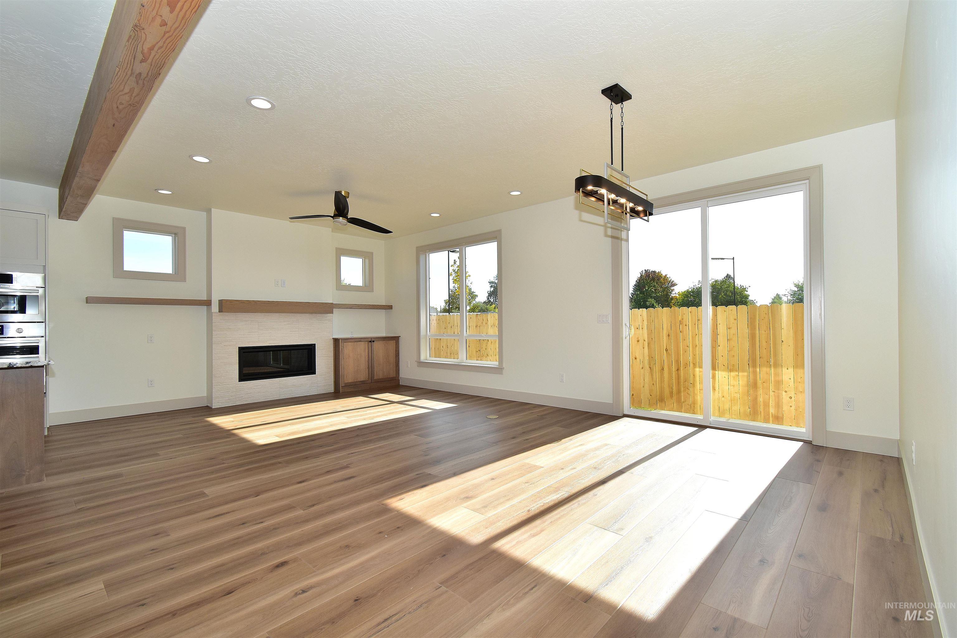 Unfurnished living room featuring healthy amount of natural light, wood finished floors, a fireplace, beamed ceiling, and recessed lighting