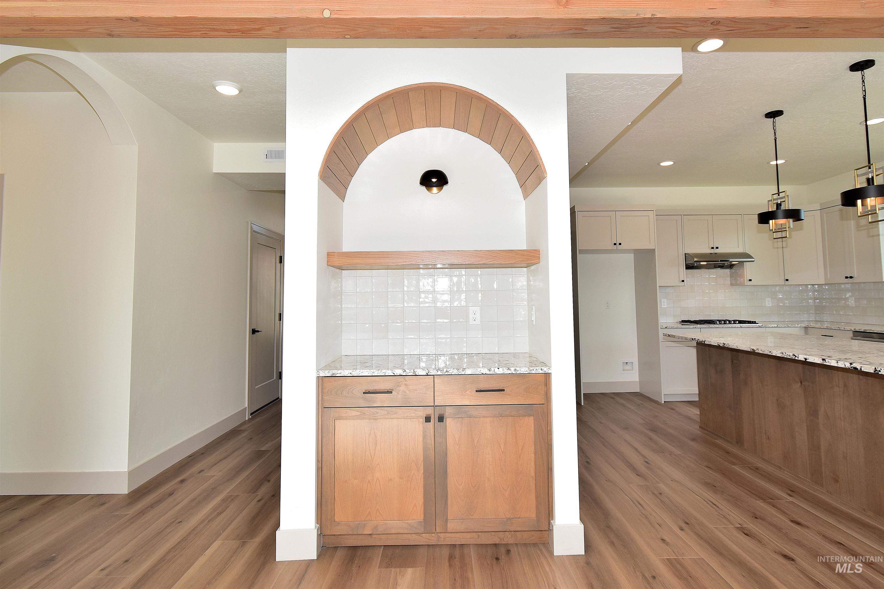 Kitchen with light stone counters, light wood-type flooring, backsplash, pendant lighting, and recessed lighting