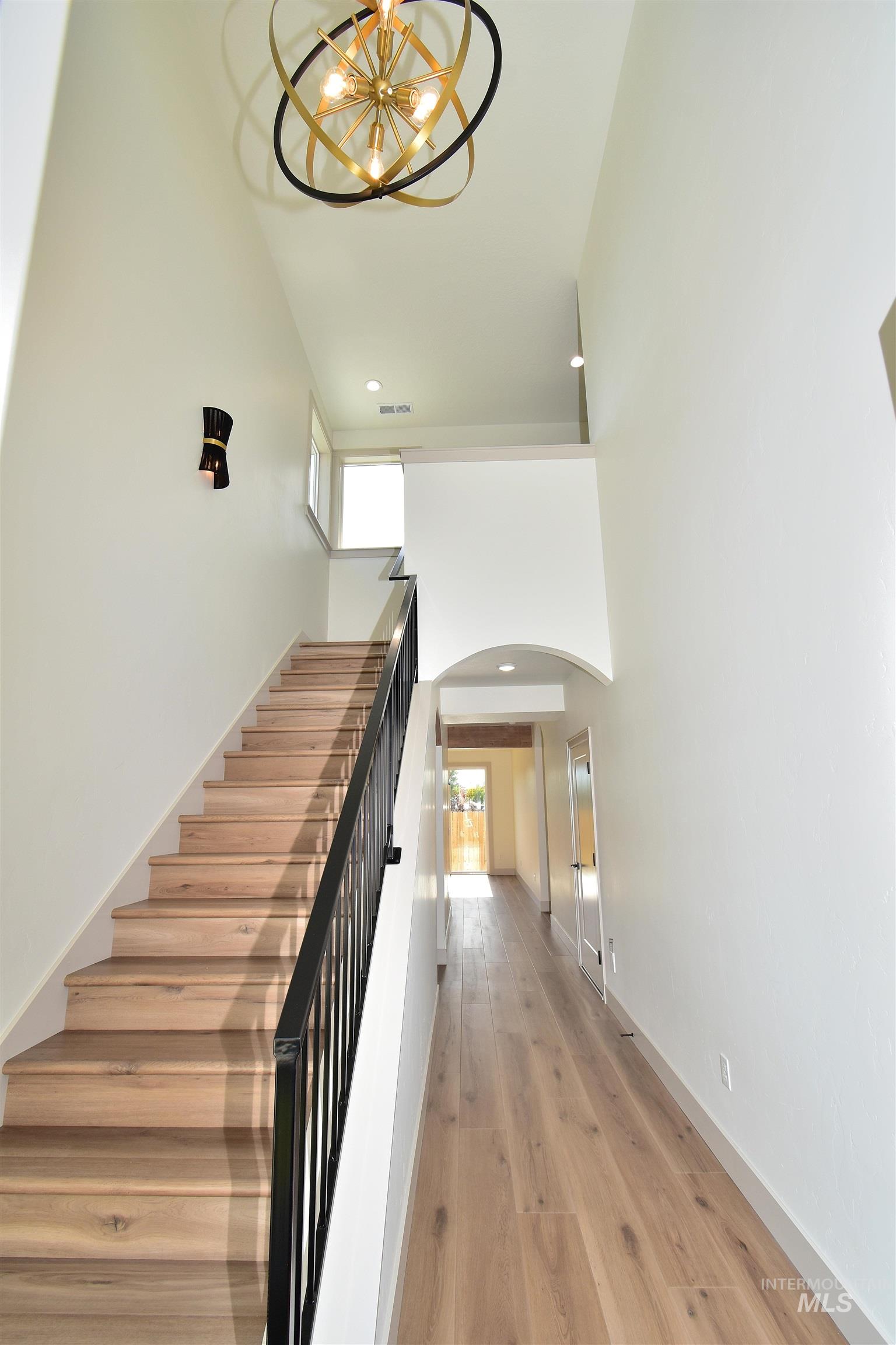 Staircase with a chandelier, arched walkways, wood finished floors, recessed lighting, and a towering ceiling