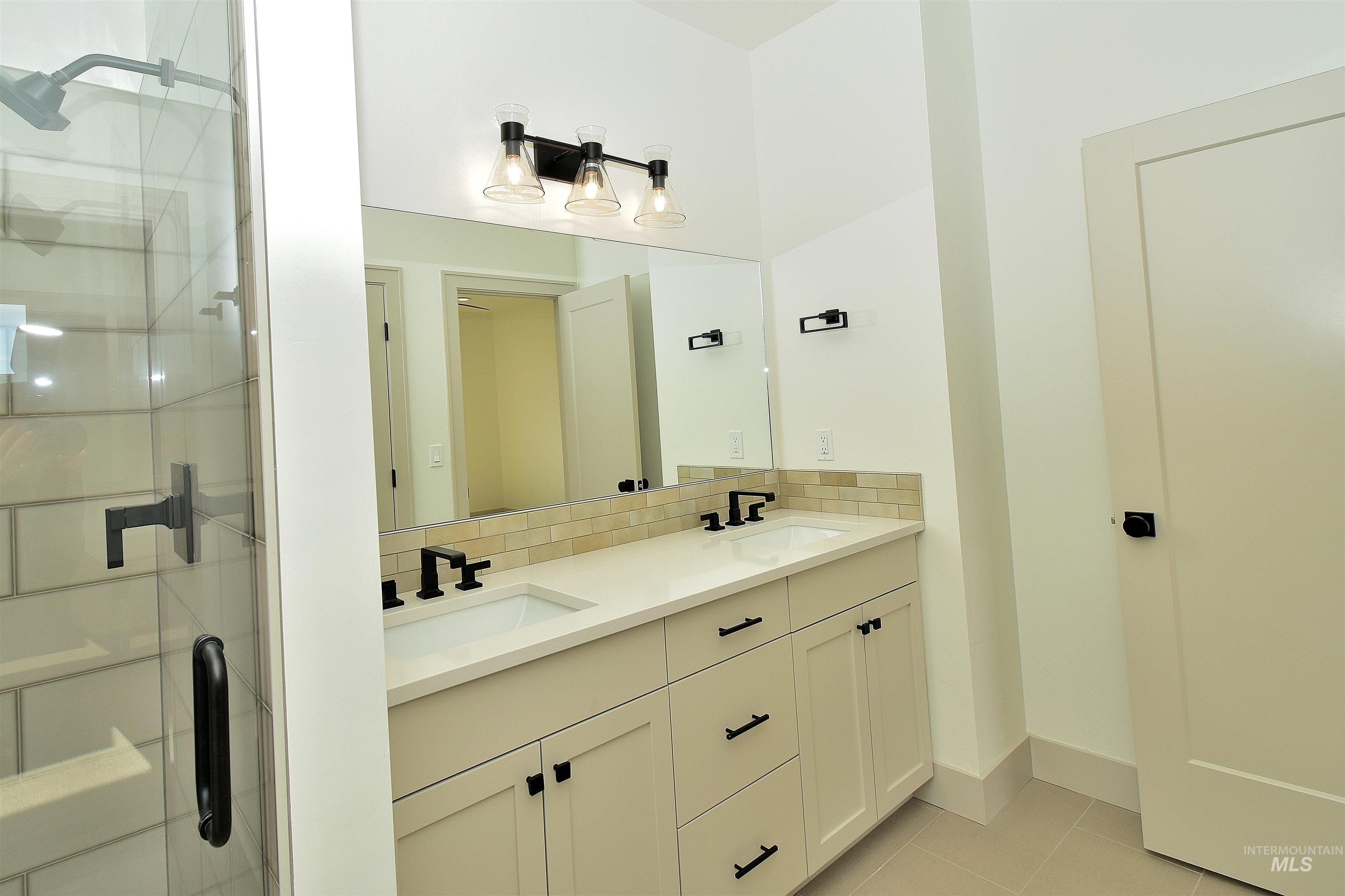 Full bath featuring light tile patterned flooring, double vanity, decorative backsplash, and a stall shower