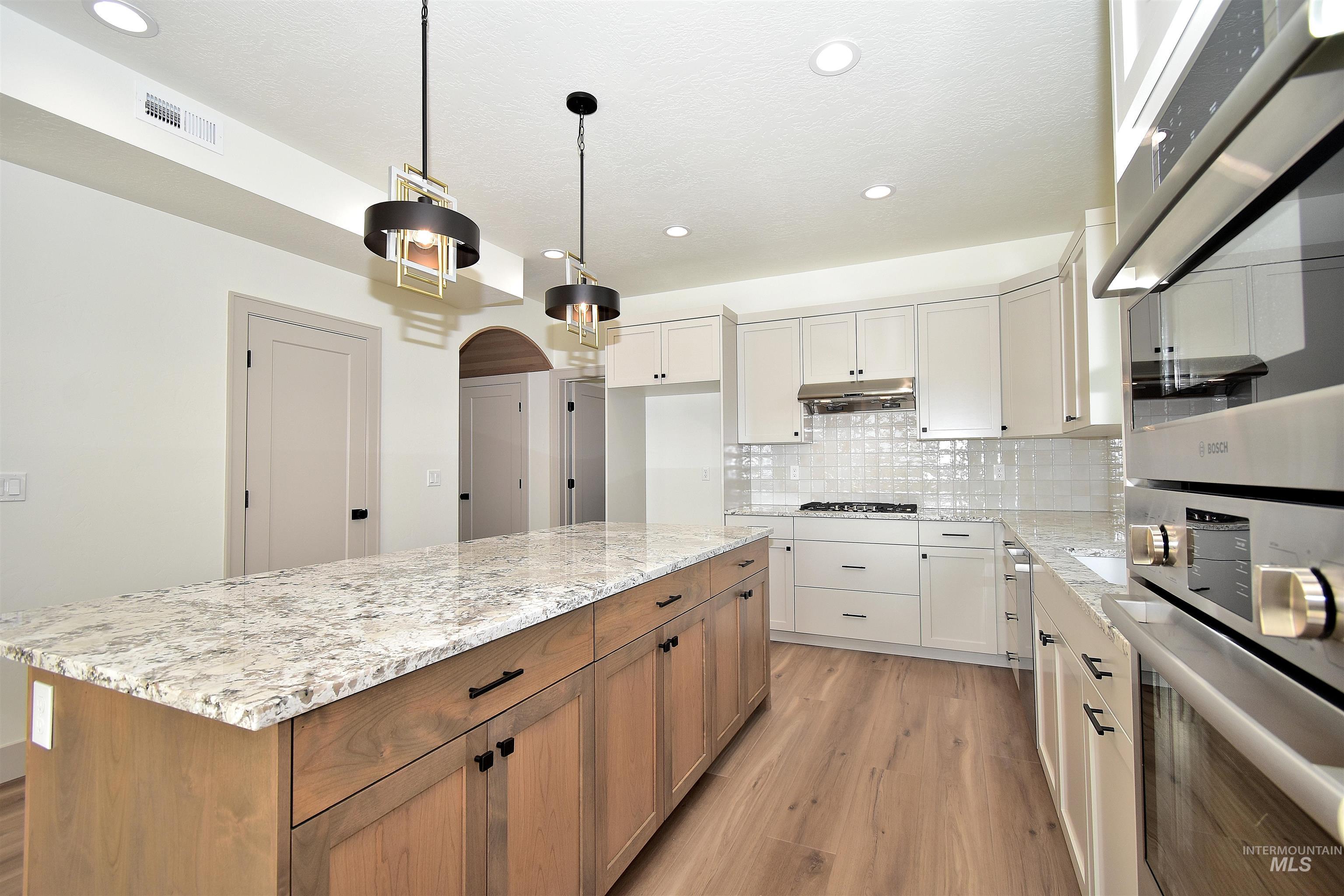 Kitchen with stainless steel double oven, light stone countertops, light wood finished floors, backsplash, and brown cabinetry