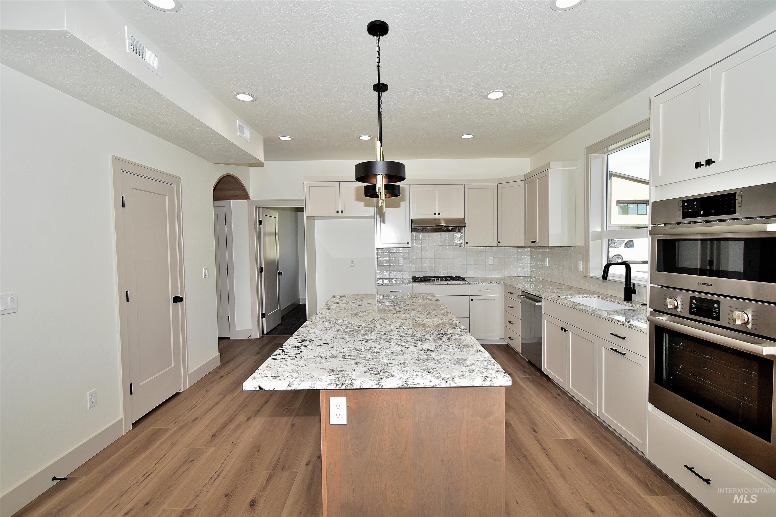 Kitchen with appliances with stainless steel finishes, a center island, light stone countertops, backsplash, and light wood-style flooring