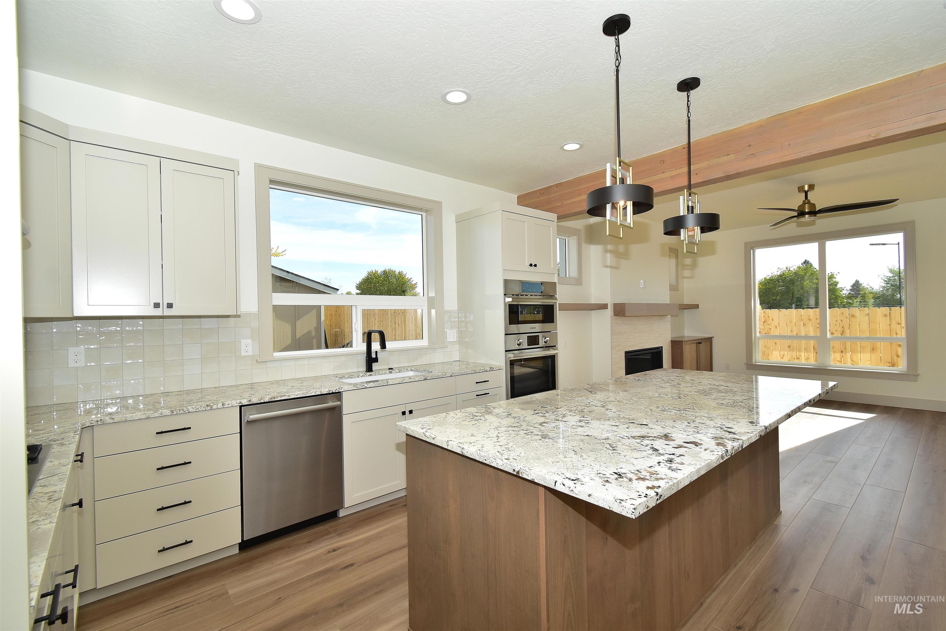 Kitchen featuring beam ceiling, healthy amount of natural light, tasteful backsplash, light stone countertops, and a kitchen island