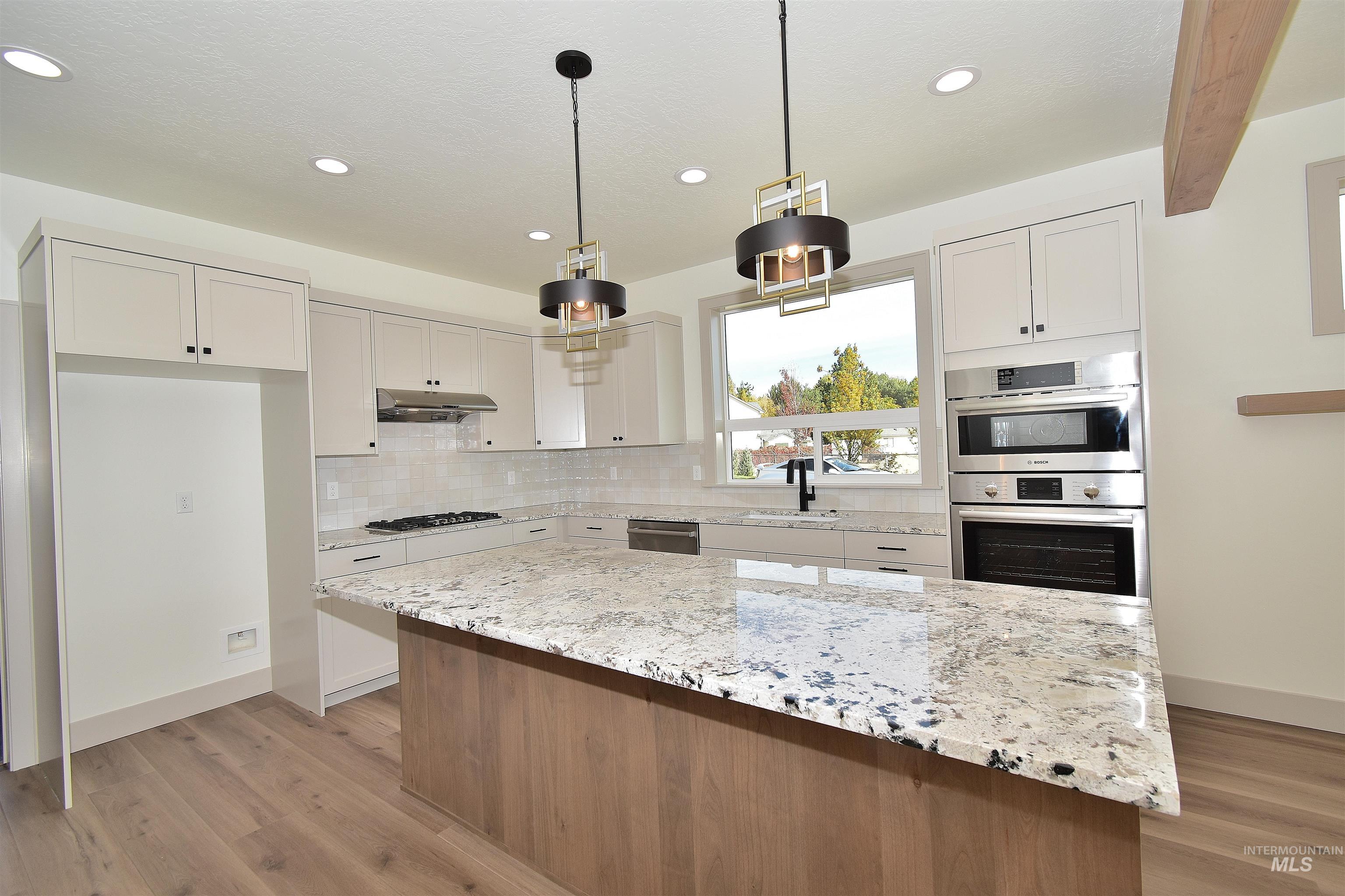 Kitchen with a center island, light wood-style floors, light stone counters, decorative light fixtures, and decorative backsplash