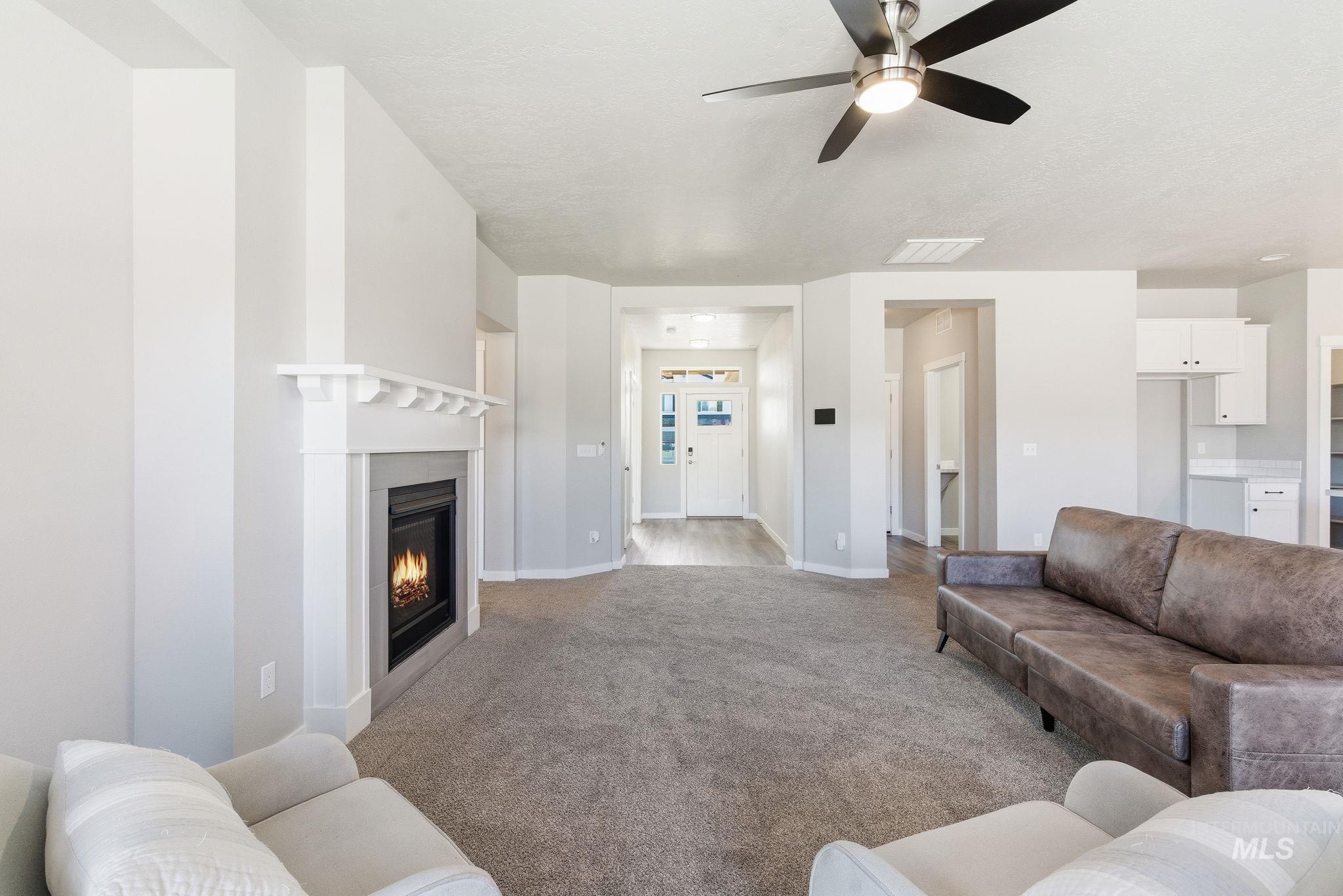 Carpeted living area with a glass covered fireplace and a ceiling fan