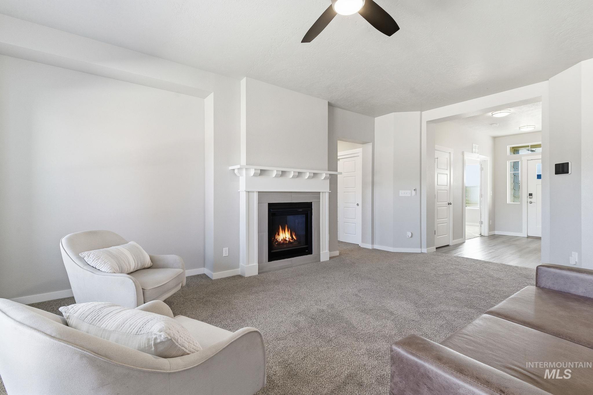 Living area featuring carpet, a glass covered fireplace, and a ceiling fan