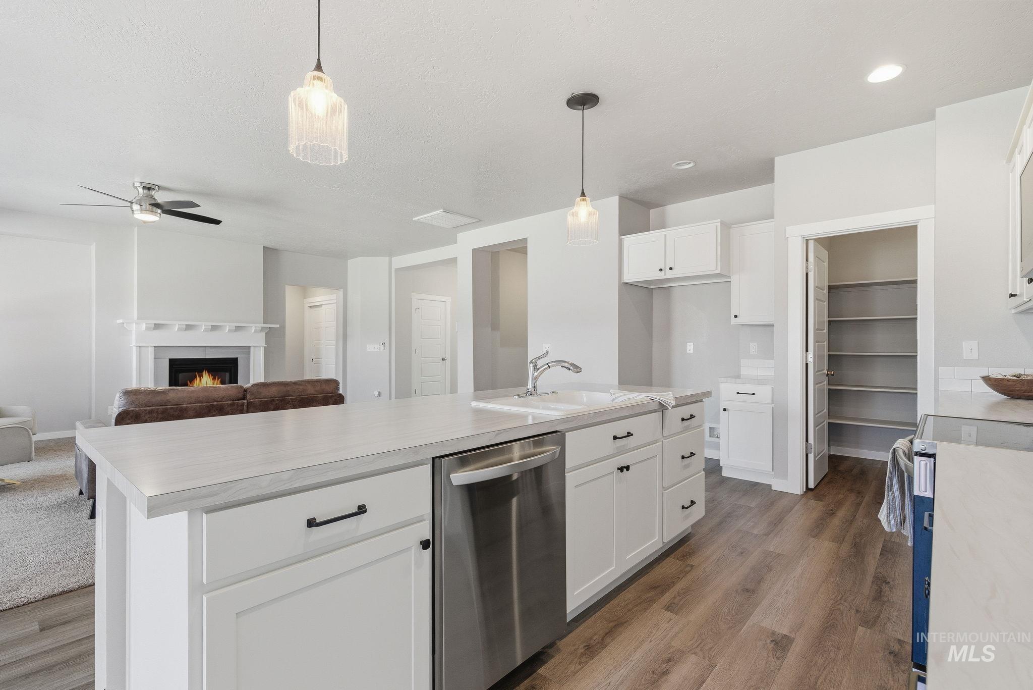 Kitchen with light countertops, stainless steel dishwasher, a warm lit fireplace, ceiling fan, and decorative light fixtures