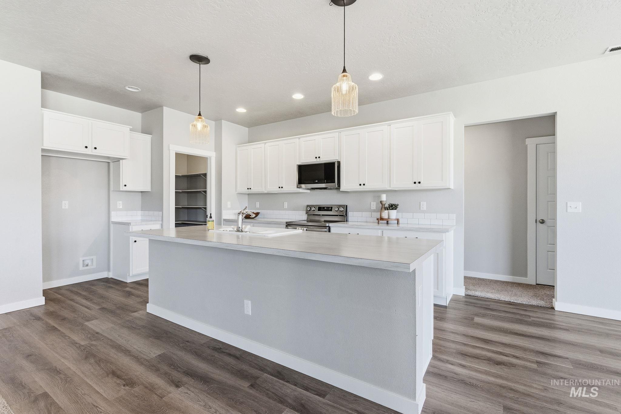 Kitchen with light countertops, white cabinetry, hanging light fixtures, stainless steel appliances, and recessed lighting