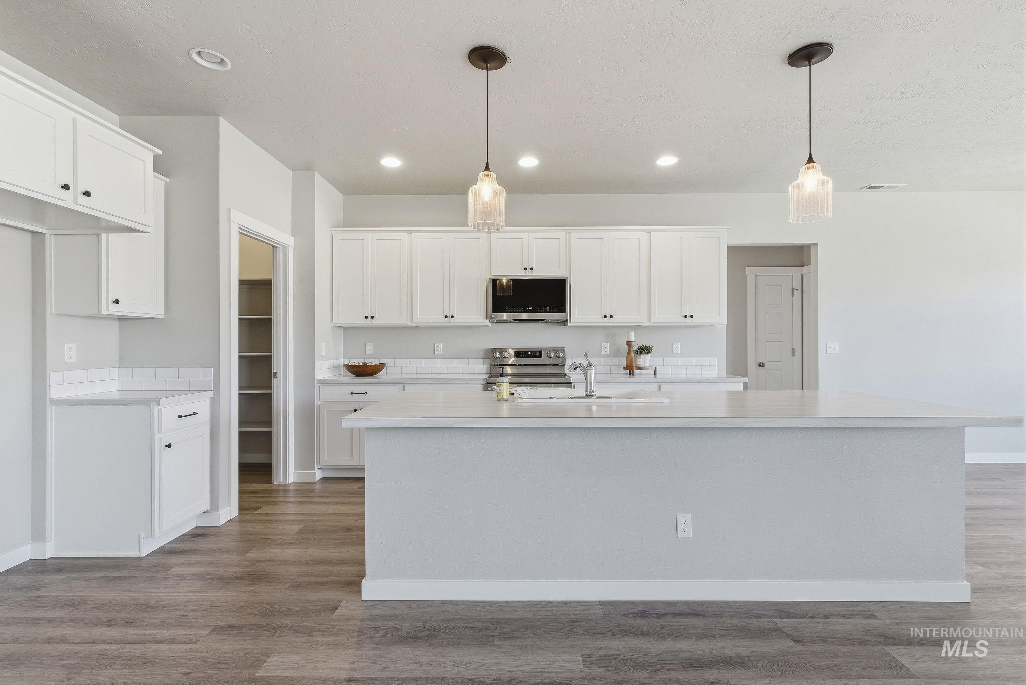 Kitchen featuring white cabinetry, light wood-type flooring, pendant lighting, appliances with stainless steel finishes, and recessed lighting