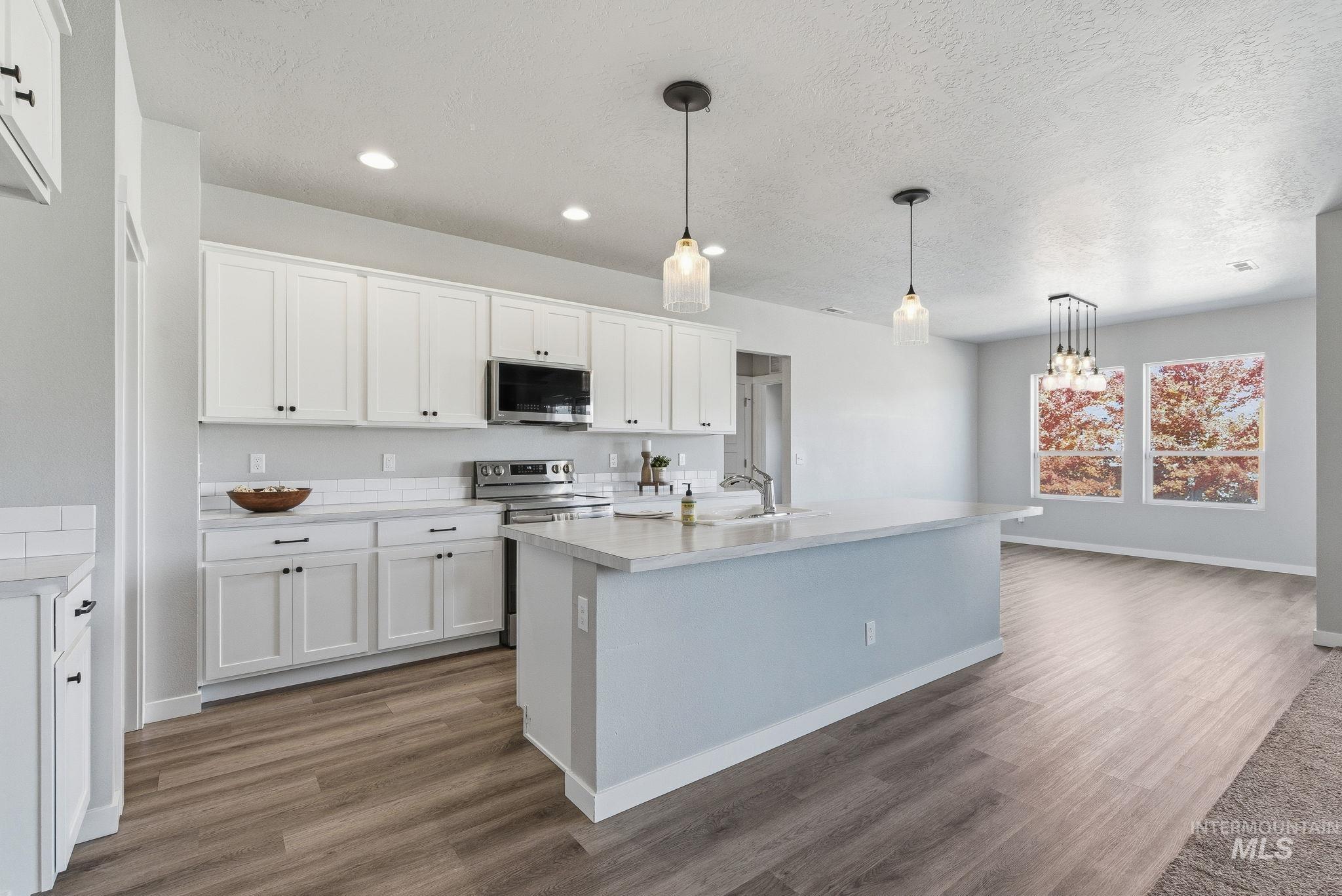Kitchen featuring decorative light fixtures, light countertops, white cabinetry, light wood finished floors, and a textured ceiling