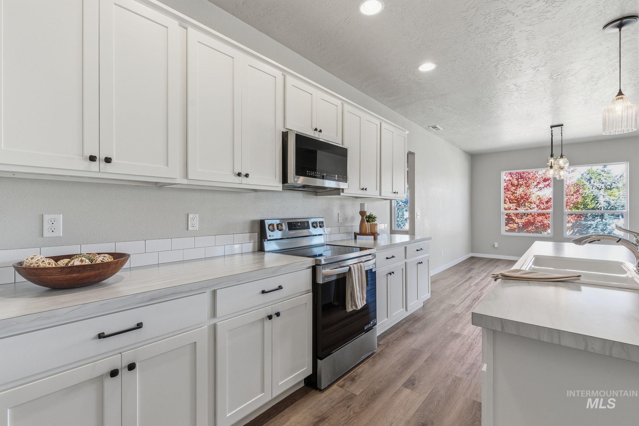 Kitchen with light countertops, stainless steel appliances, white cabinetry, hanging light fixtures, and a textured ceiling