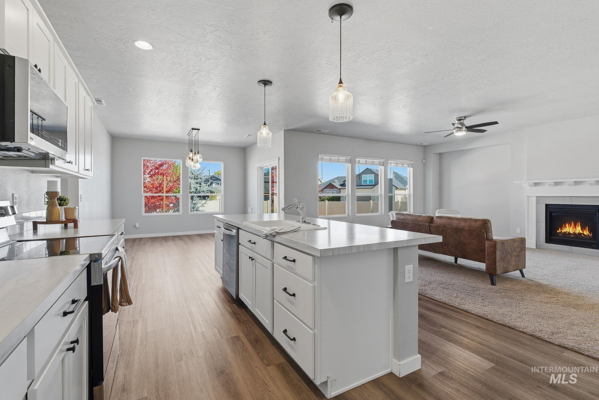 Kitchen featuring white cabinetry, appliances with stainless steel finishes, a fireplace, hanging light fixtures, and a textured ceiling