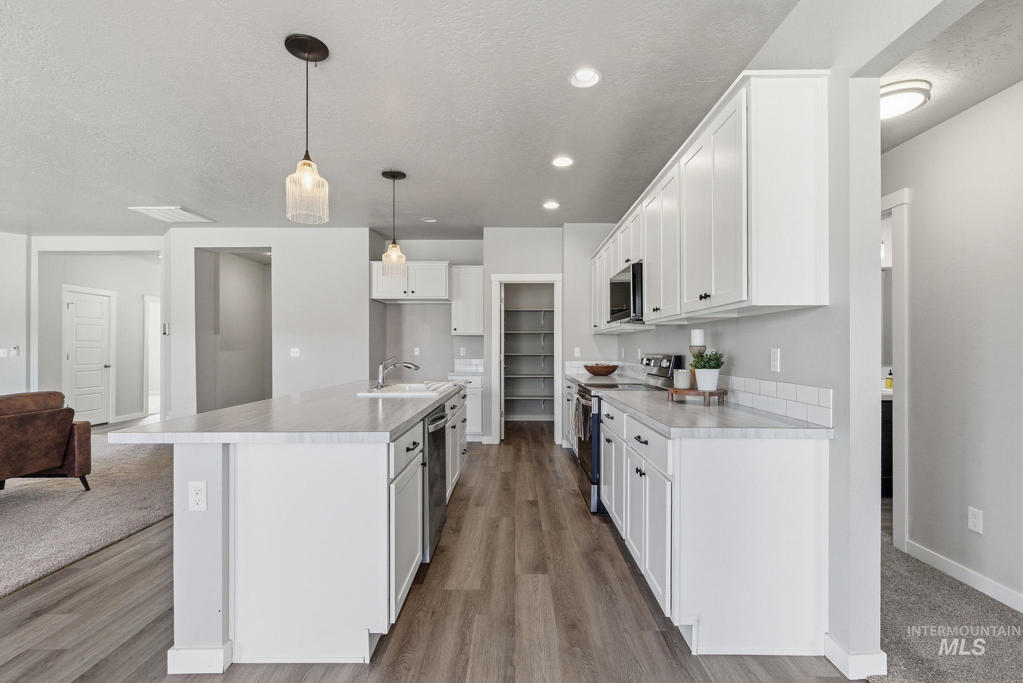 Kitchen featuring light countertops, a textured ceiling, appliances with stainless steel finishes, a kitchen island with sink, and white cabinetry