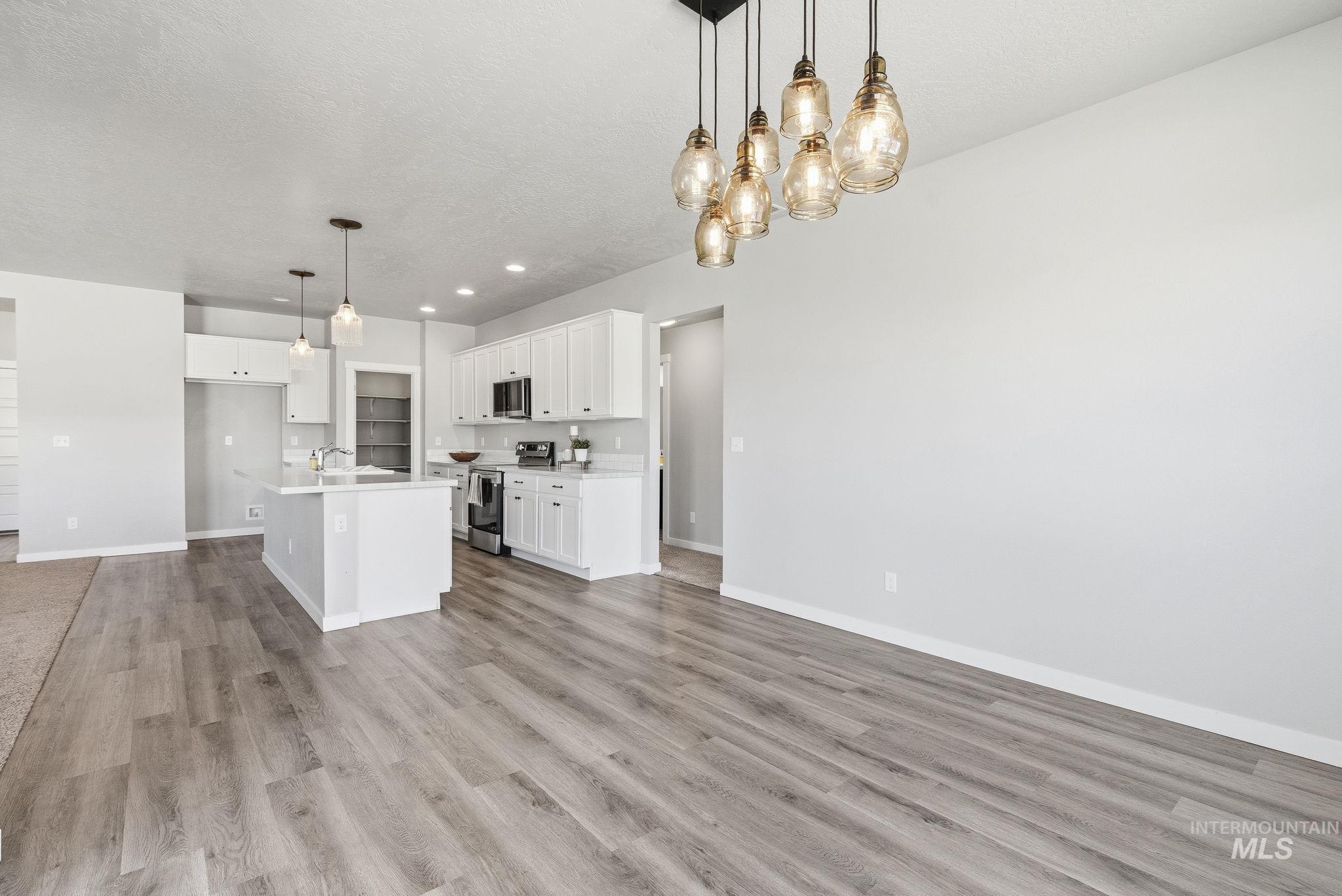 Kitchen with decorative light fixtures, appliances with stainless steel finishes, white cabinets, open floor plan, and a textured ceiling