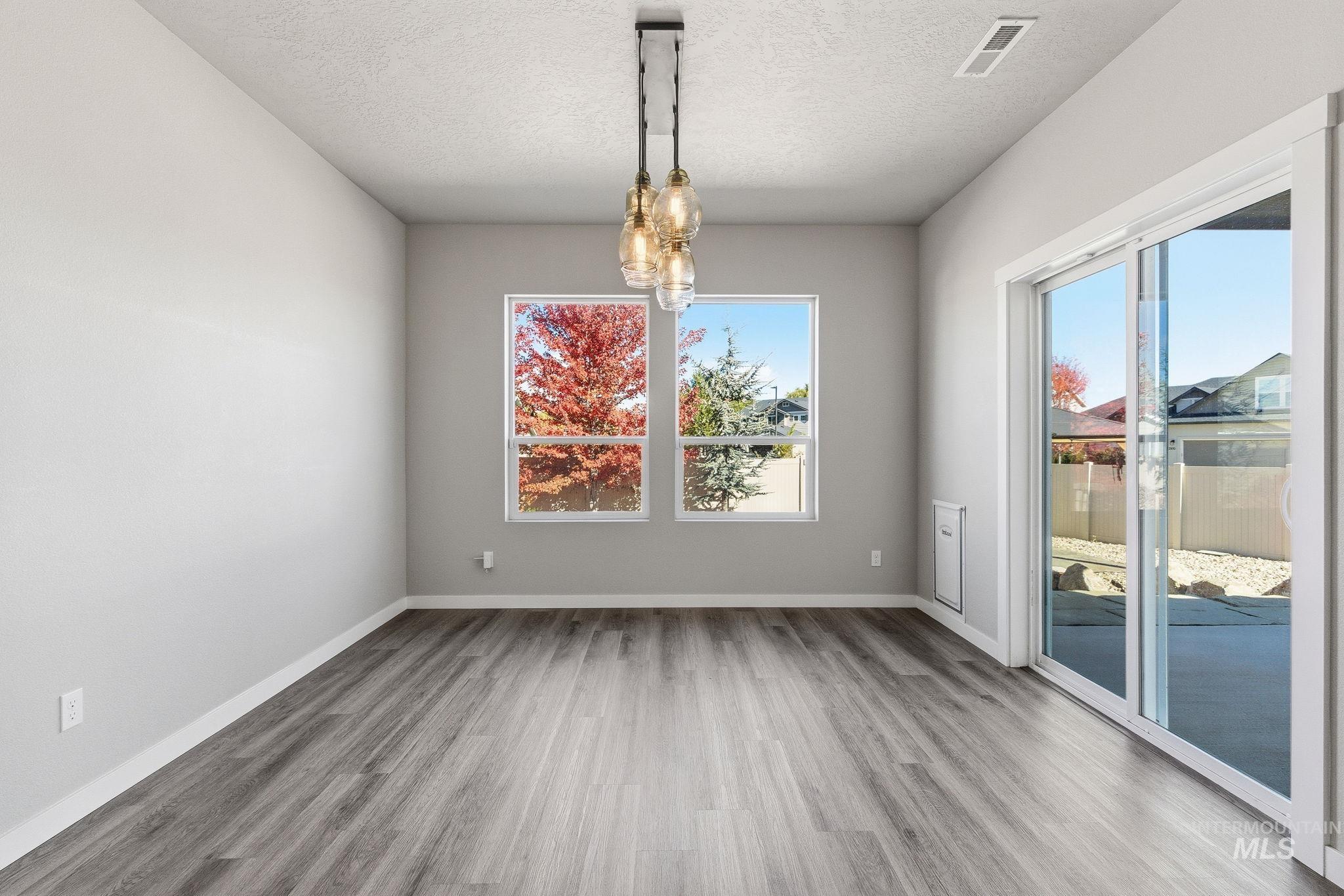 Unfurnished dining area featuring light wood finished floors, a textured ceiling, and a chandelier