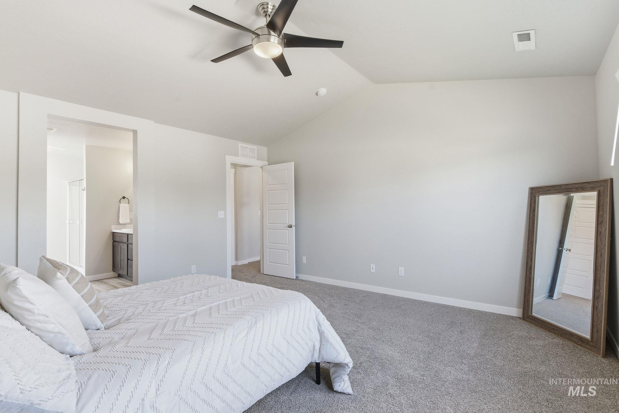 Carpeted bedroom with vaulted ceiling, ensuite bath, and a ceiling fan