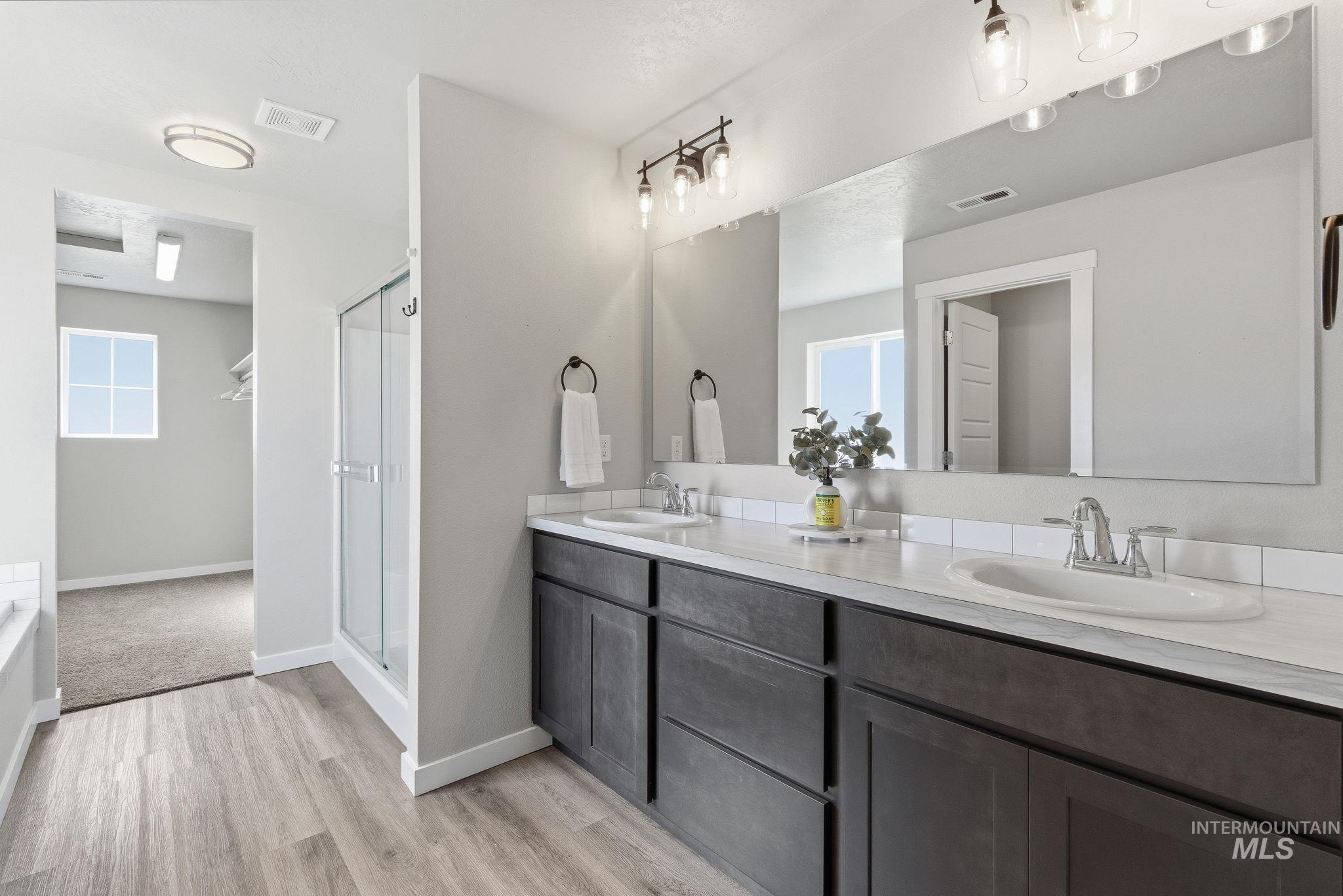Bathroom featuring double vanity, light wood-style floors, a stall shower, and a tub