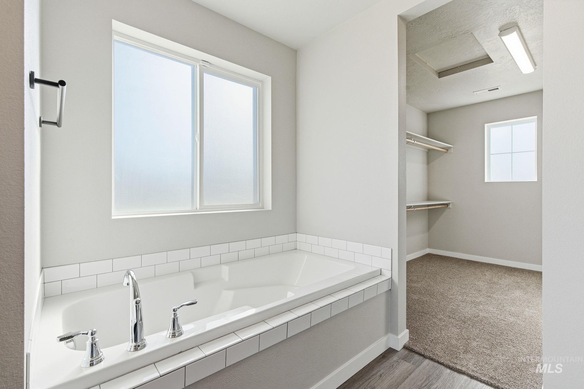 Bathroom featuring a garden tub, a walk in closet, and wood finished floors
