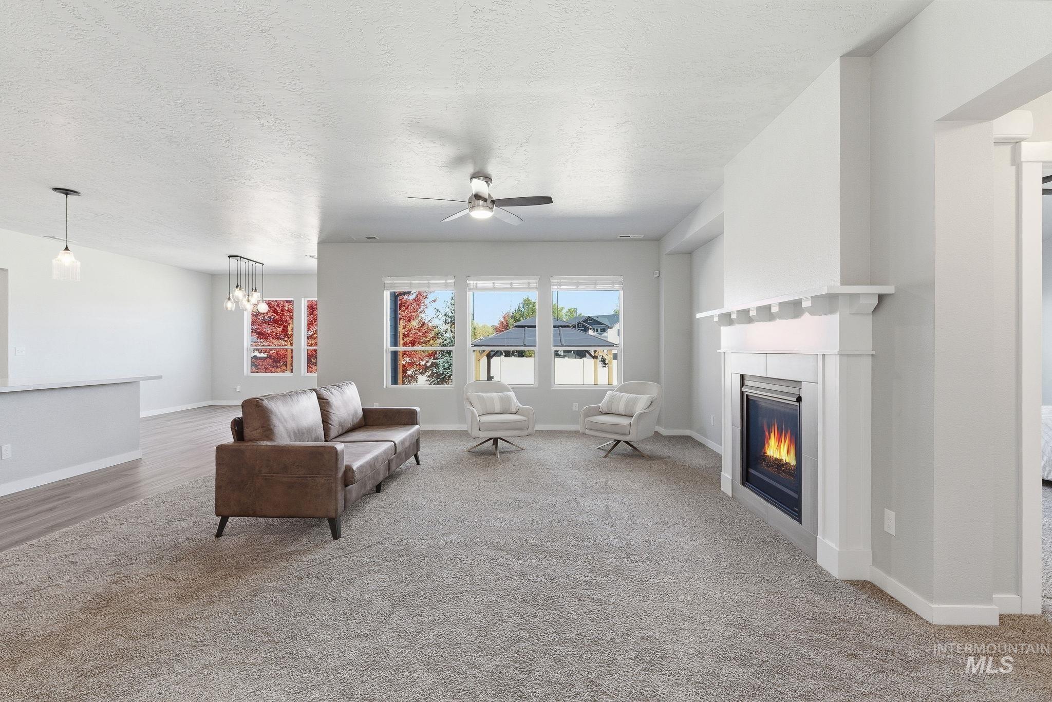 Living room featuring light colored carpet, a glass covered fireplace, a ceiling fan, a textured ceiling, and a chandelier