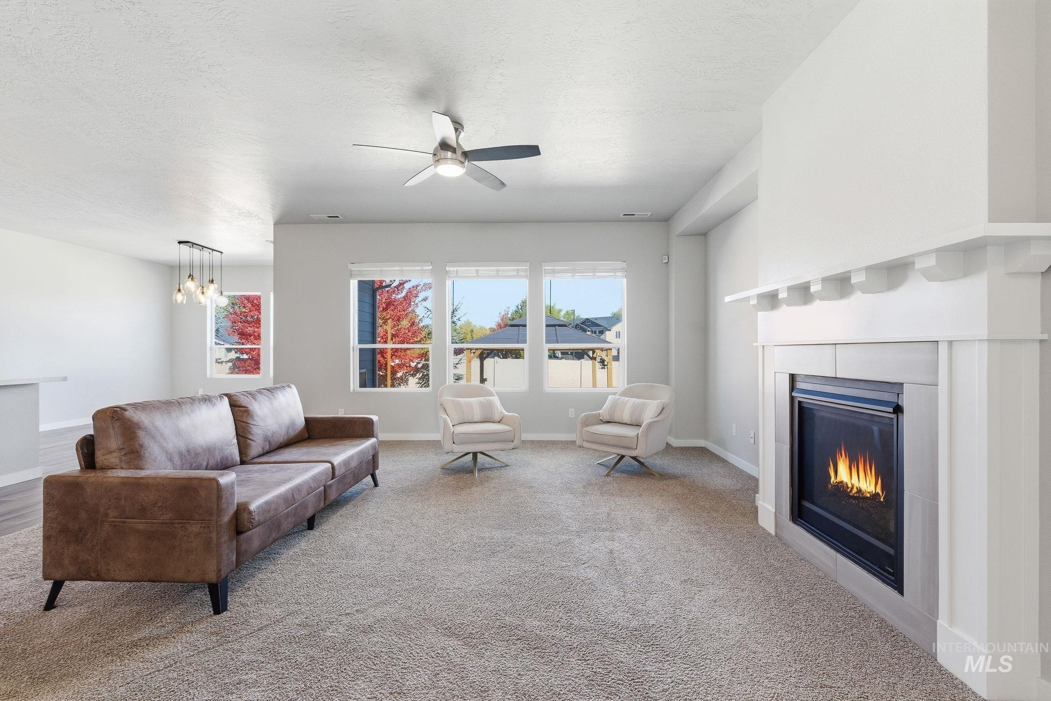 Living room featuring a glass covered fireplace, carpet floors, a textured ceiling, a ceiling fan, and a chandelier