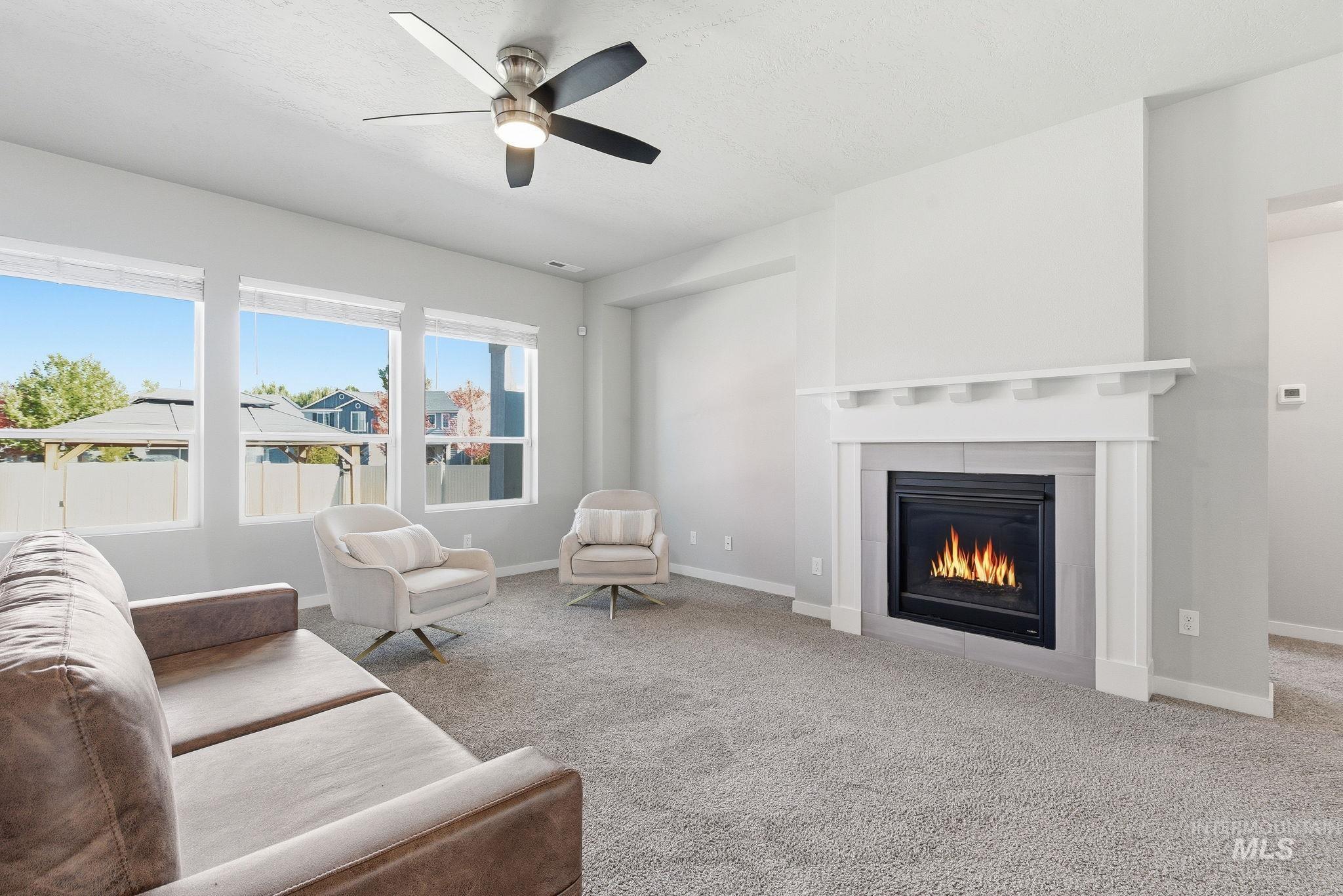 Carpeted living area featuring a glass covered fireplace and a ceiling fan