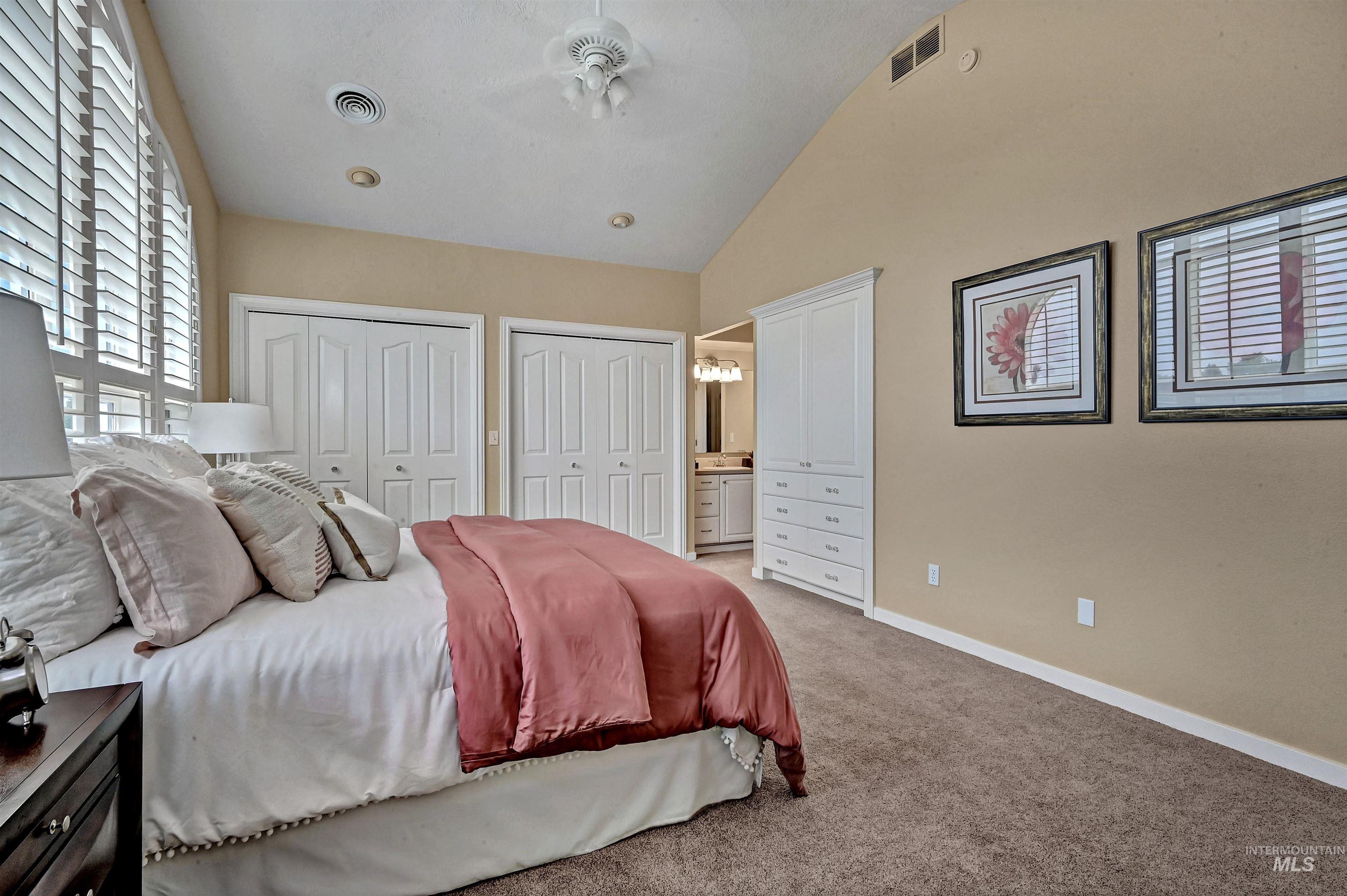 Bedroom with two closets, lofted ceiling, ensuite bathroom, and light carpet