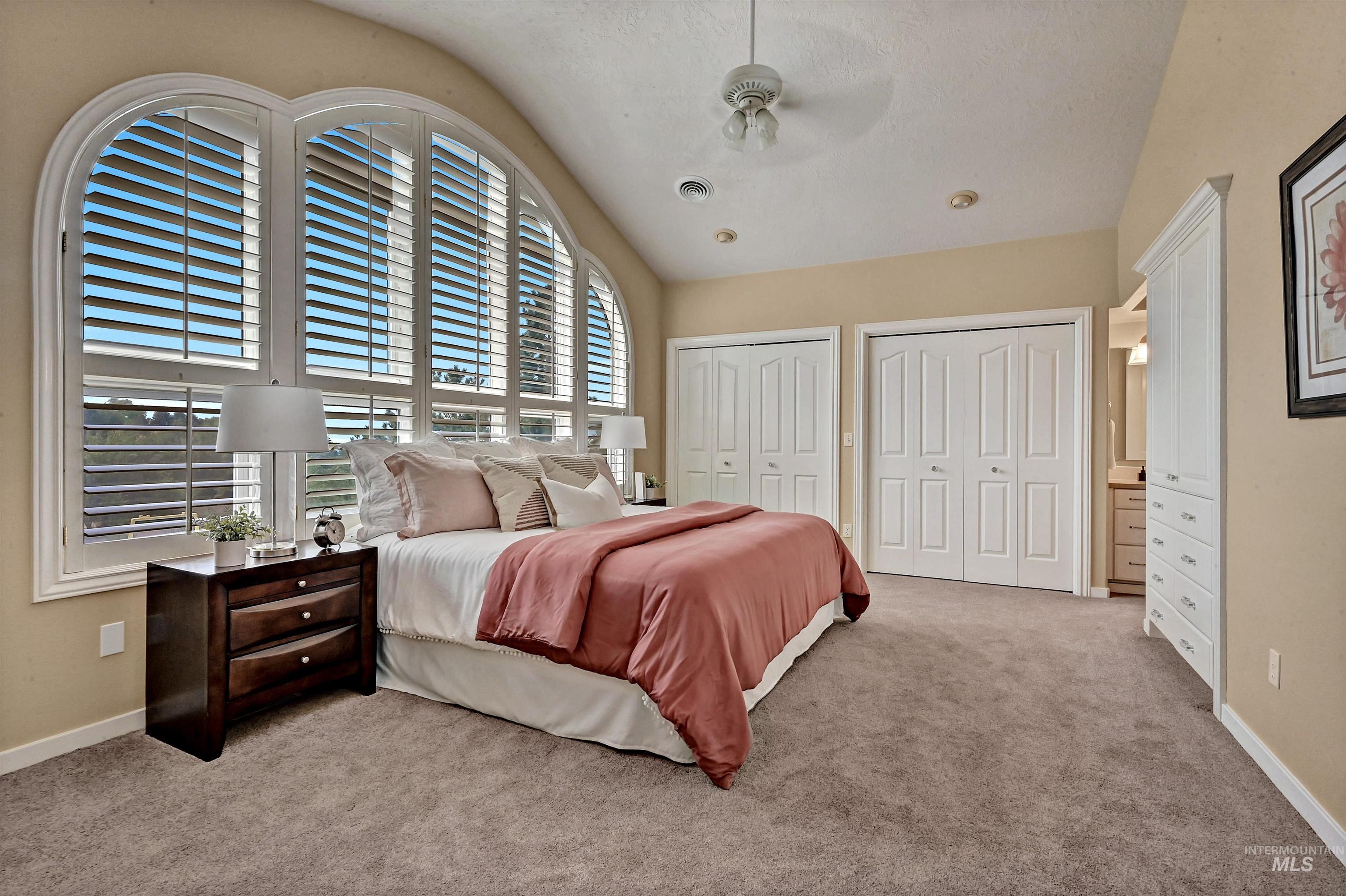 Bedroom with two closets, vaulted ceiling, light colored carpet, ceiling fan, and a textured ceiling