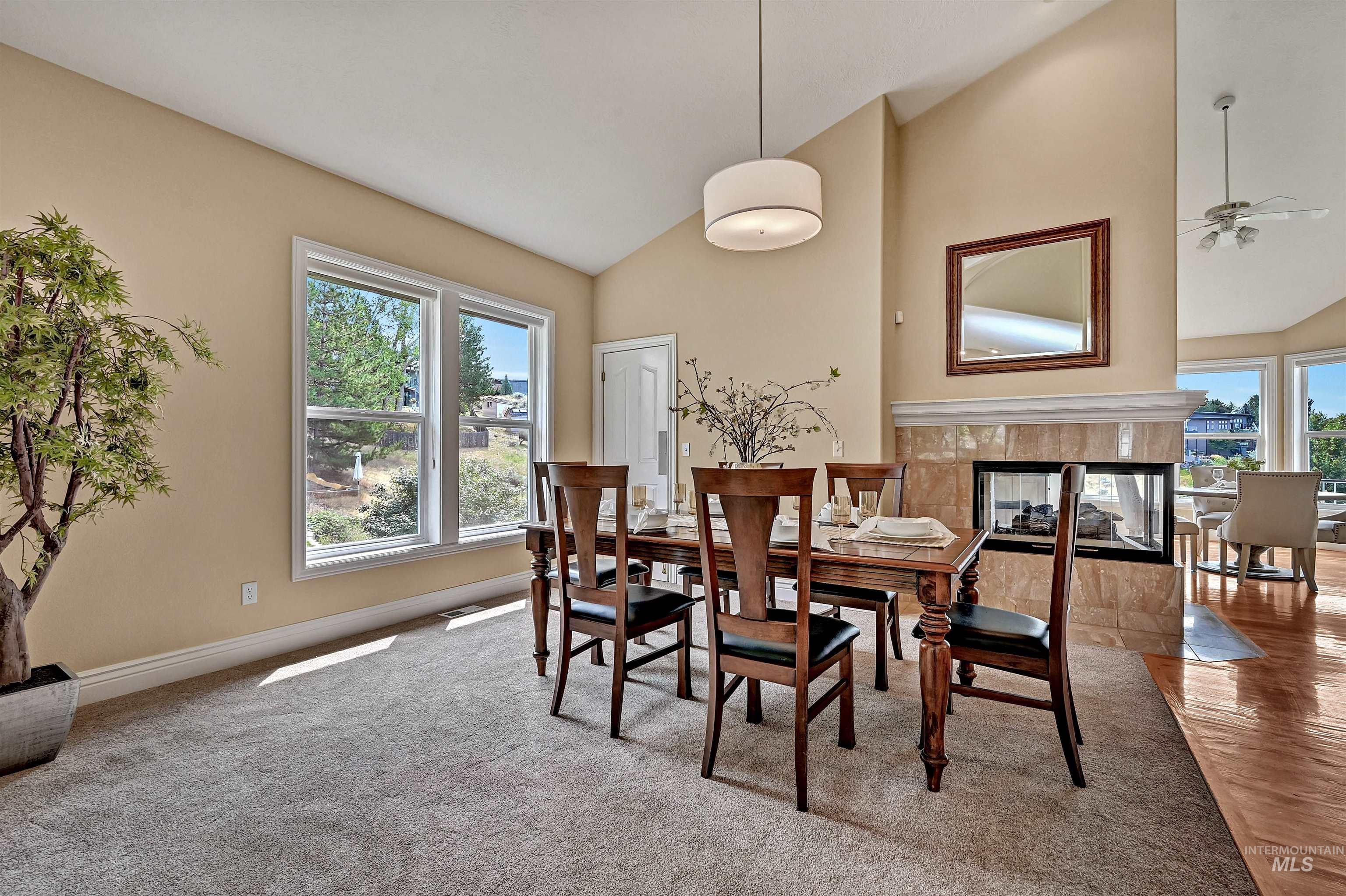 Dining room with a tiled fireplace, high vaulted ceiling, a ceiling fan, and light colored carpet