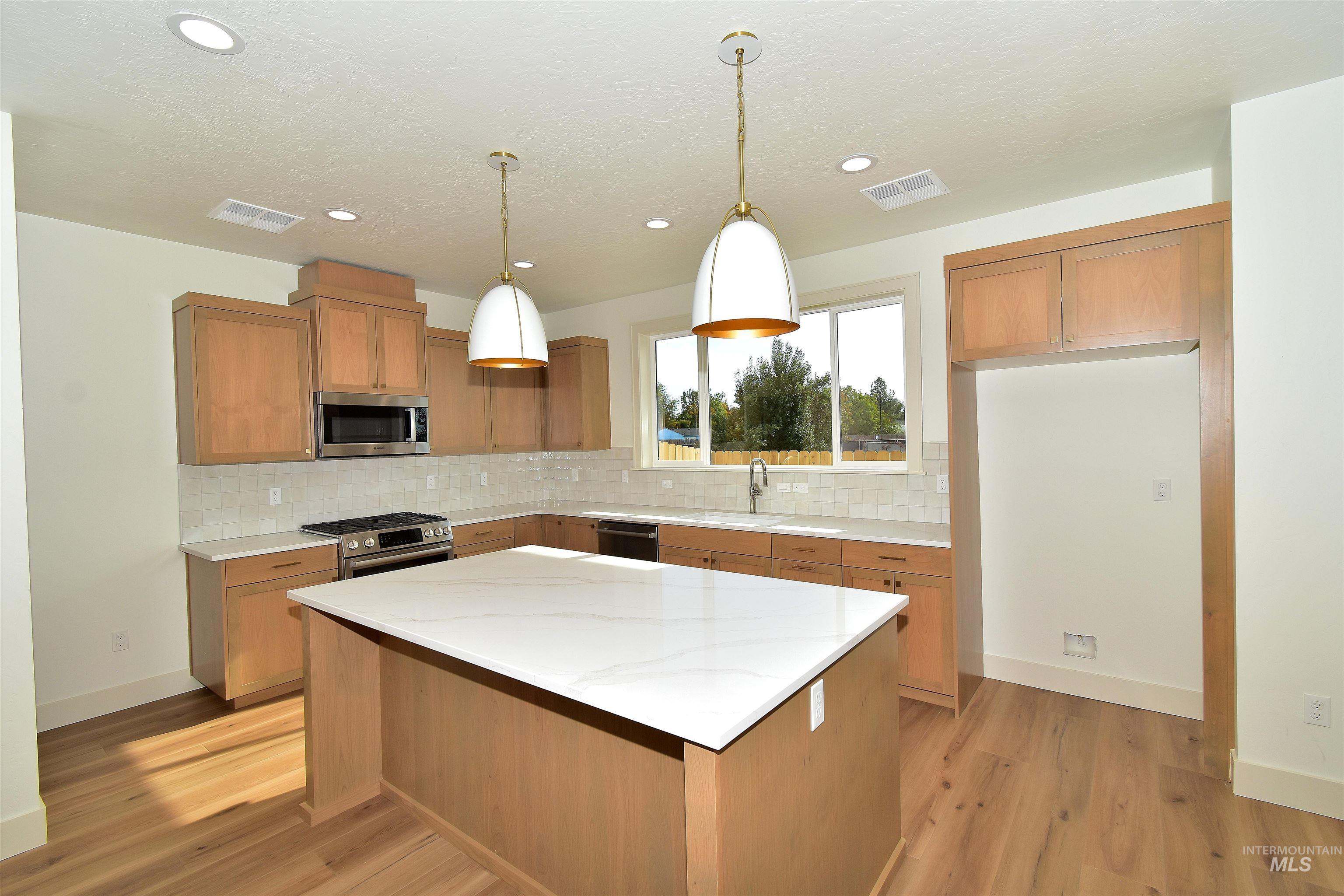 Kitchen with pendant lighting, stainless steel appliances, light stone countertops, a center island, and brown cabinetry