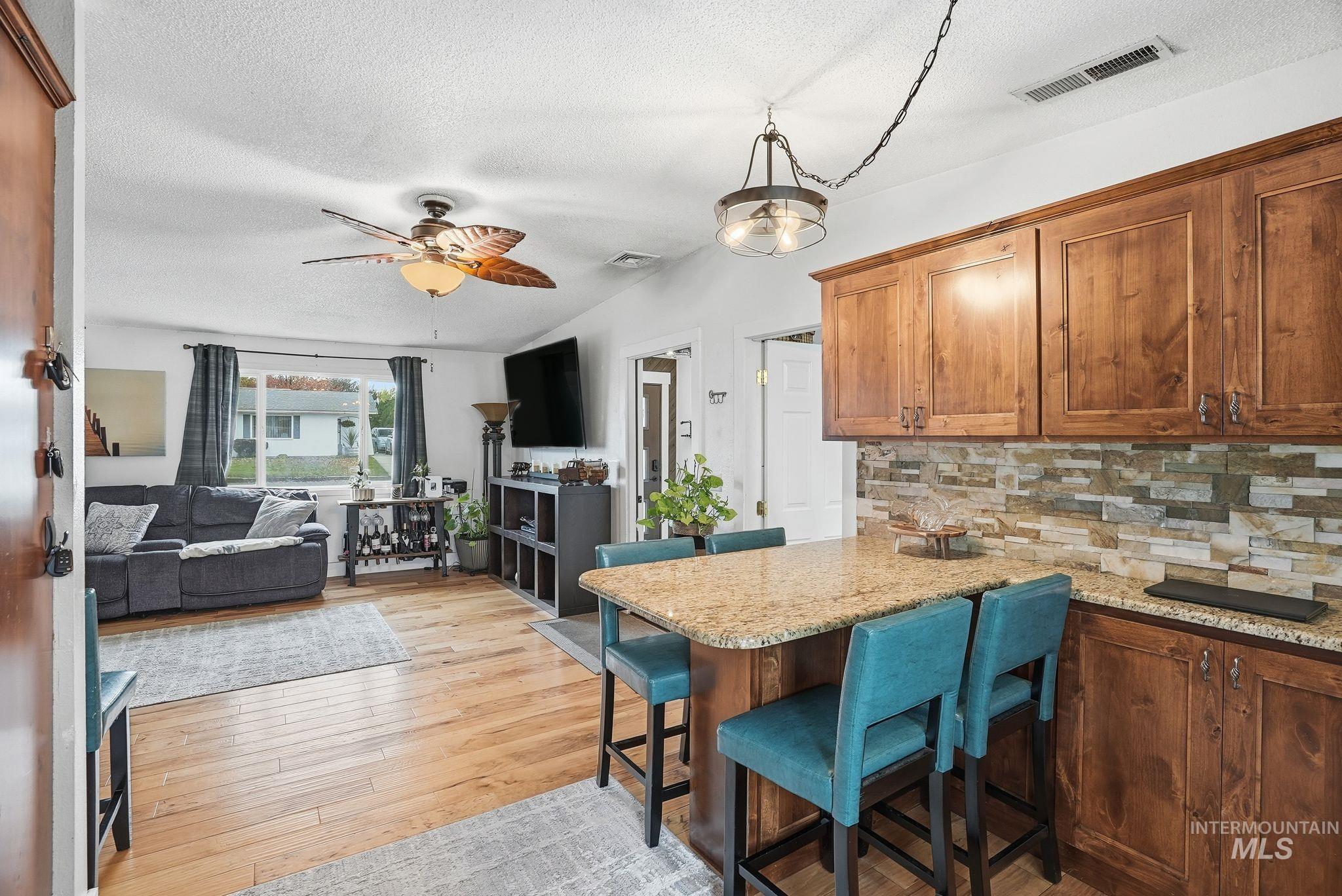 Kitchen featuring a breakfast bar area, a textured ceiling, brown cabinetry, open floor plan, and light stone countertops