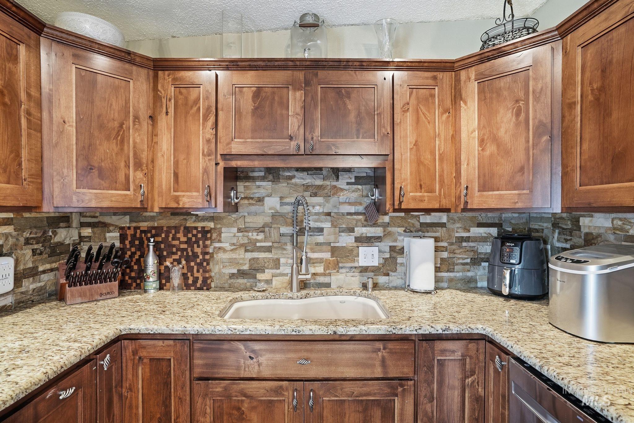 Kitchen with backsplash, light stone counters, brown cabinets, and a textured ceiling