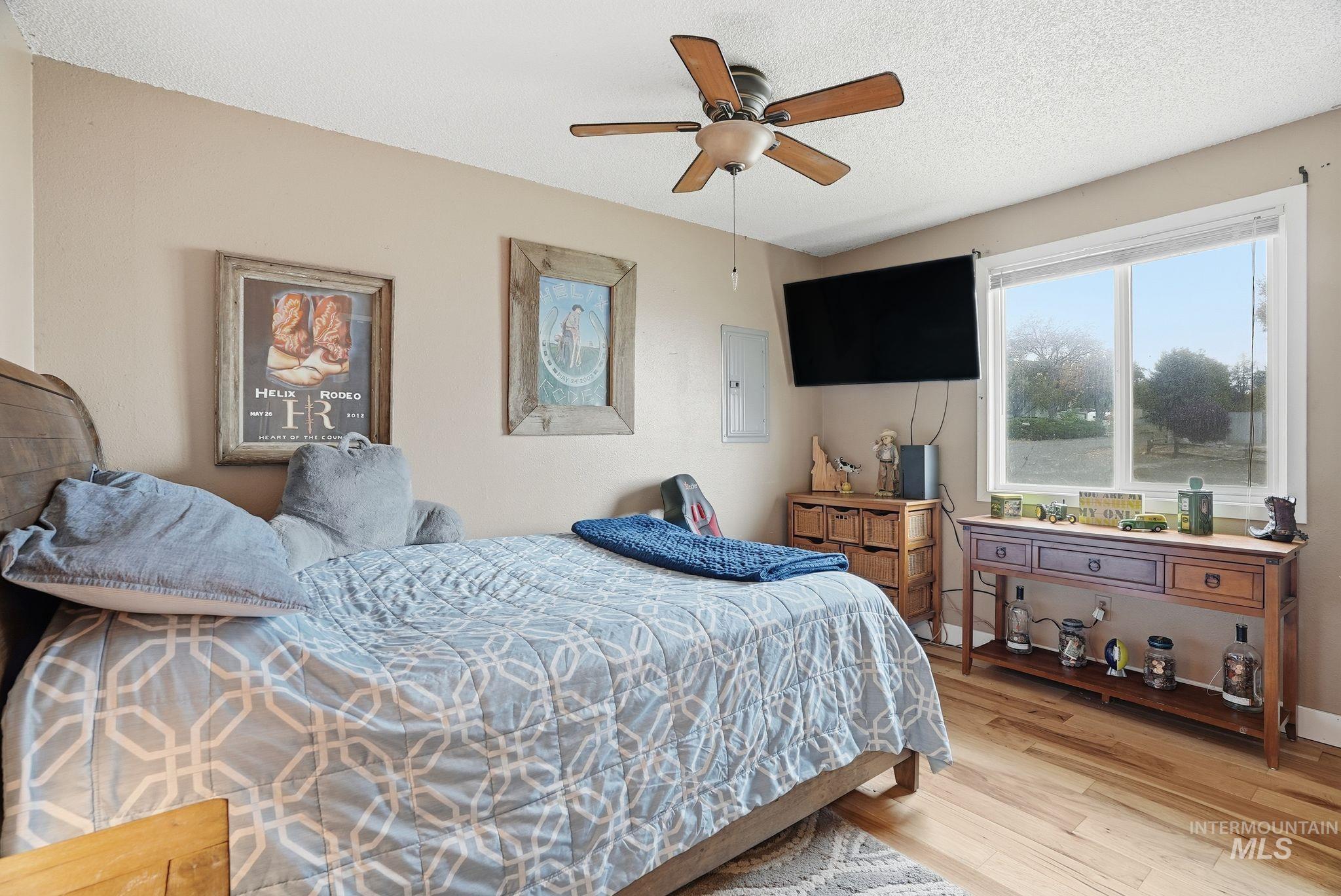 Bedroom featuring wood finished floors, a textured ceiling, ceiling fan, and electric panel