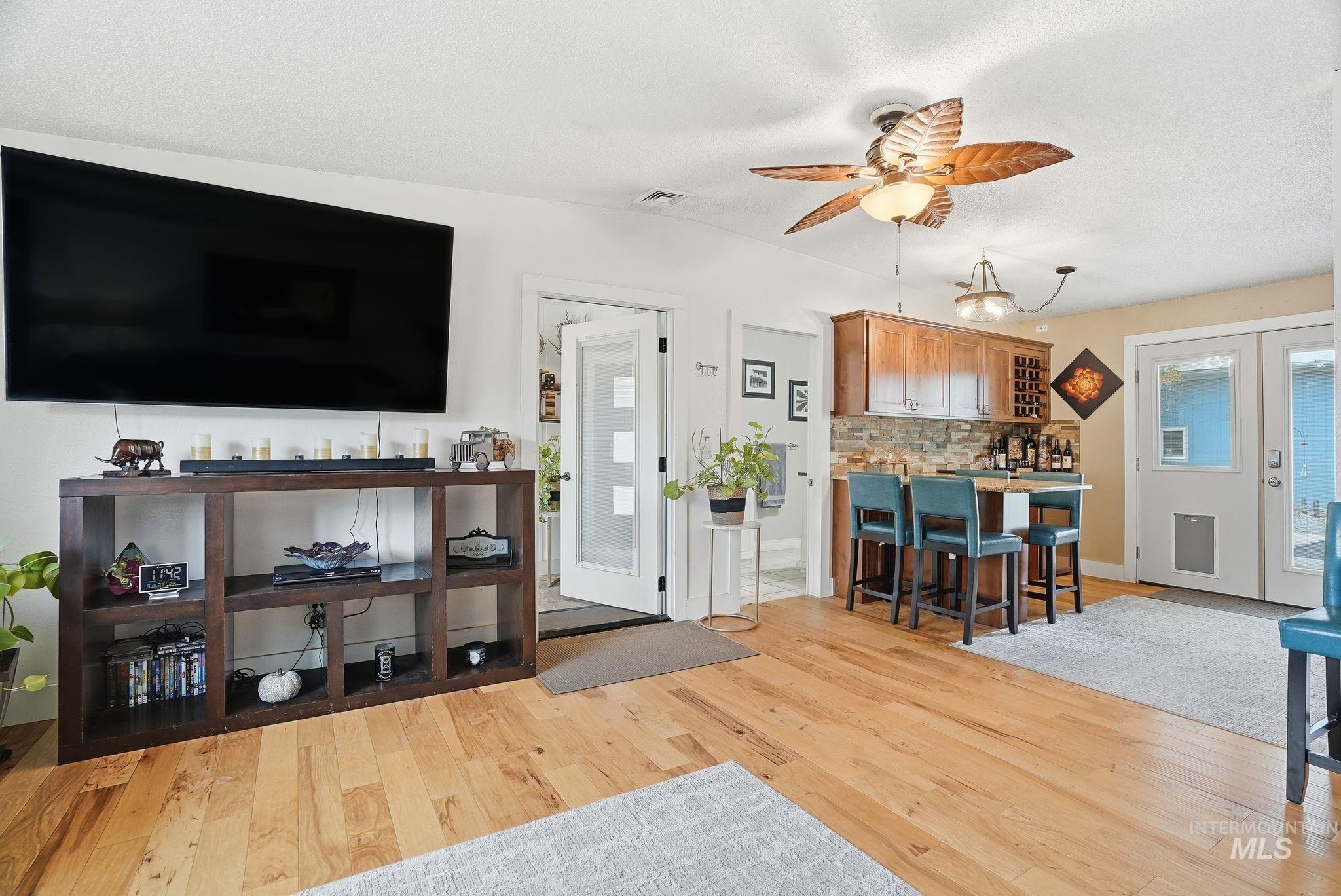 Living area with light wood-type flooring, a ceiling fan, vaulted ceiling, and a textured ceiling