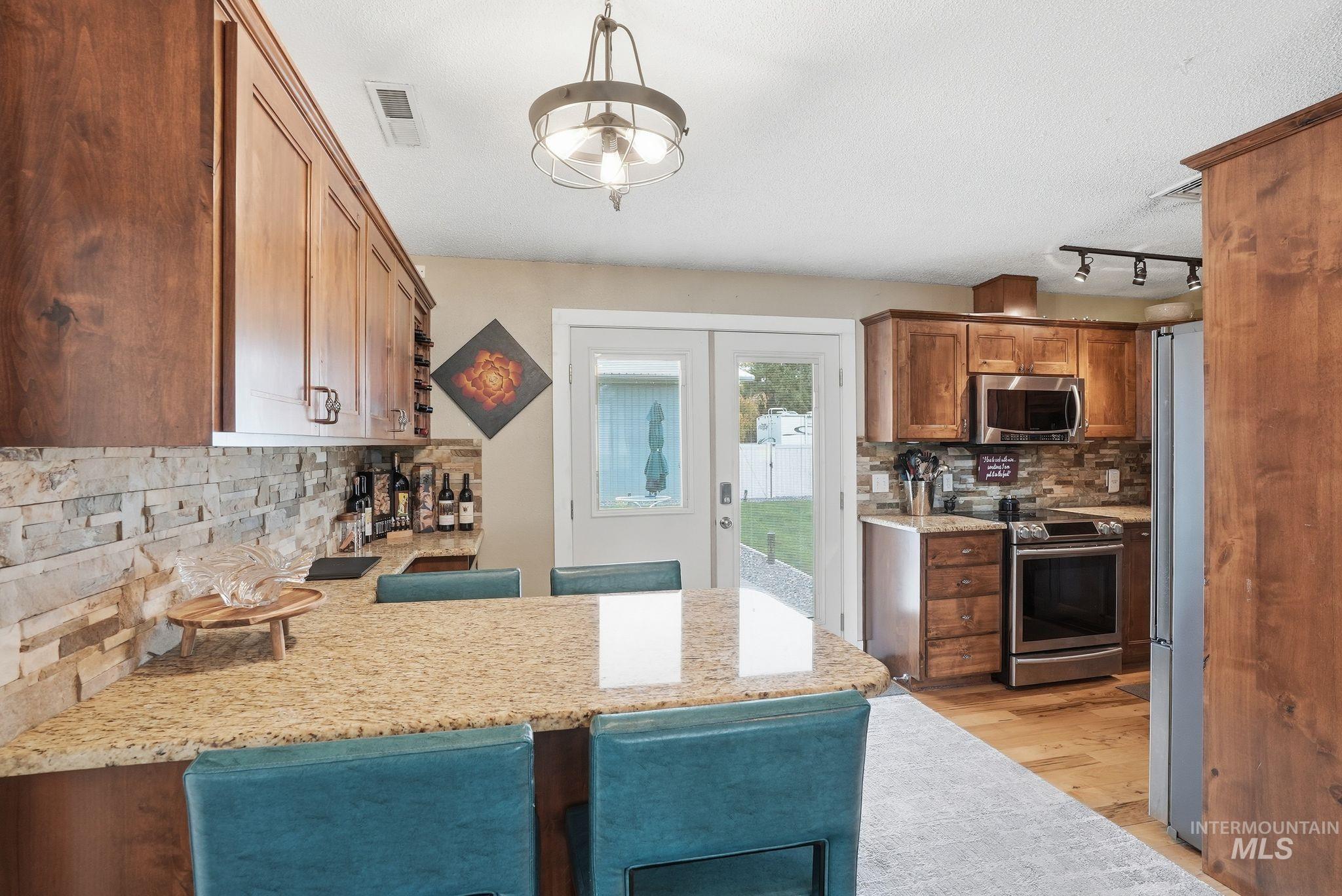 Kitchen featuring tasteful backsplash, a kitchen bar, stainless steel appliances, a peninsula, and light stone countertops