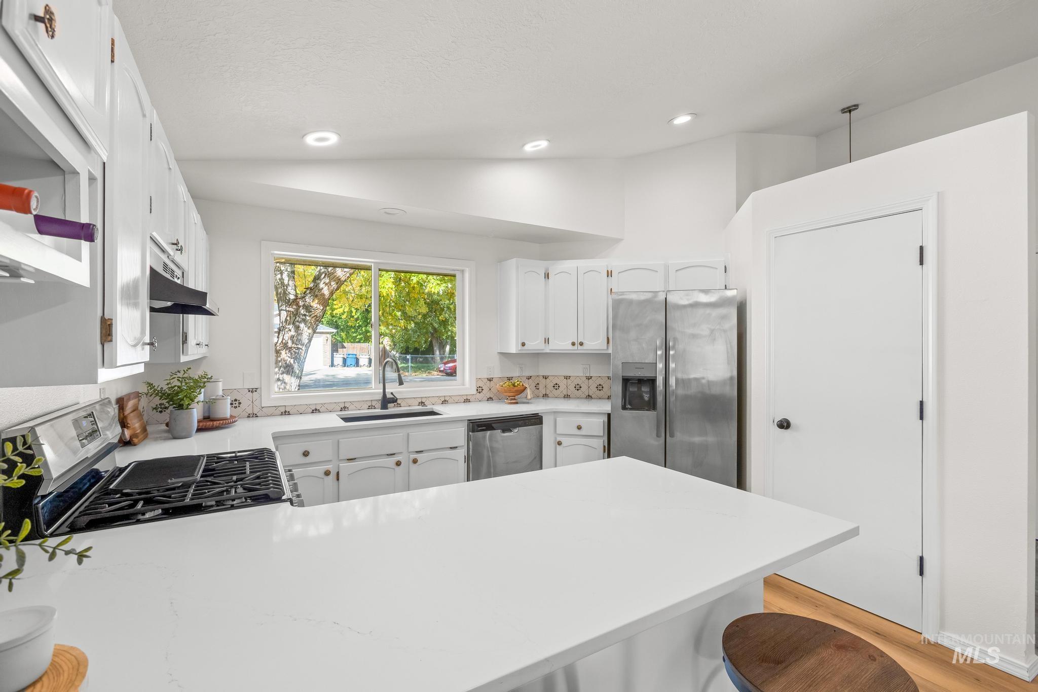 Kitchen with white cabinets, a kitchen breakfast bar, vaulted ceiling, appliances with stainless steel finishes, and a peninsula