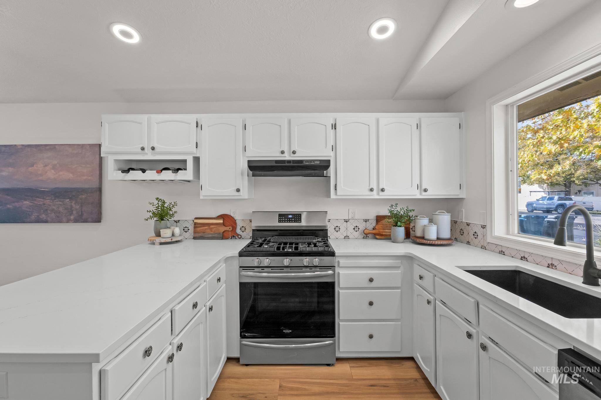 Kitchen with white cabinetry, appliances with stainless steel finishes, recessed lighting, light wood-type flooring, and a peninsula