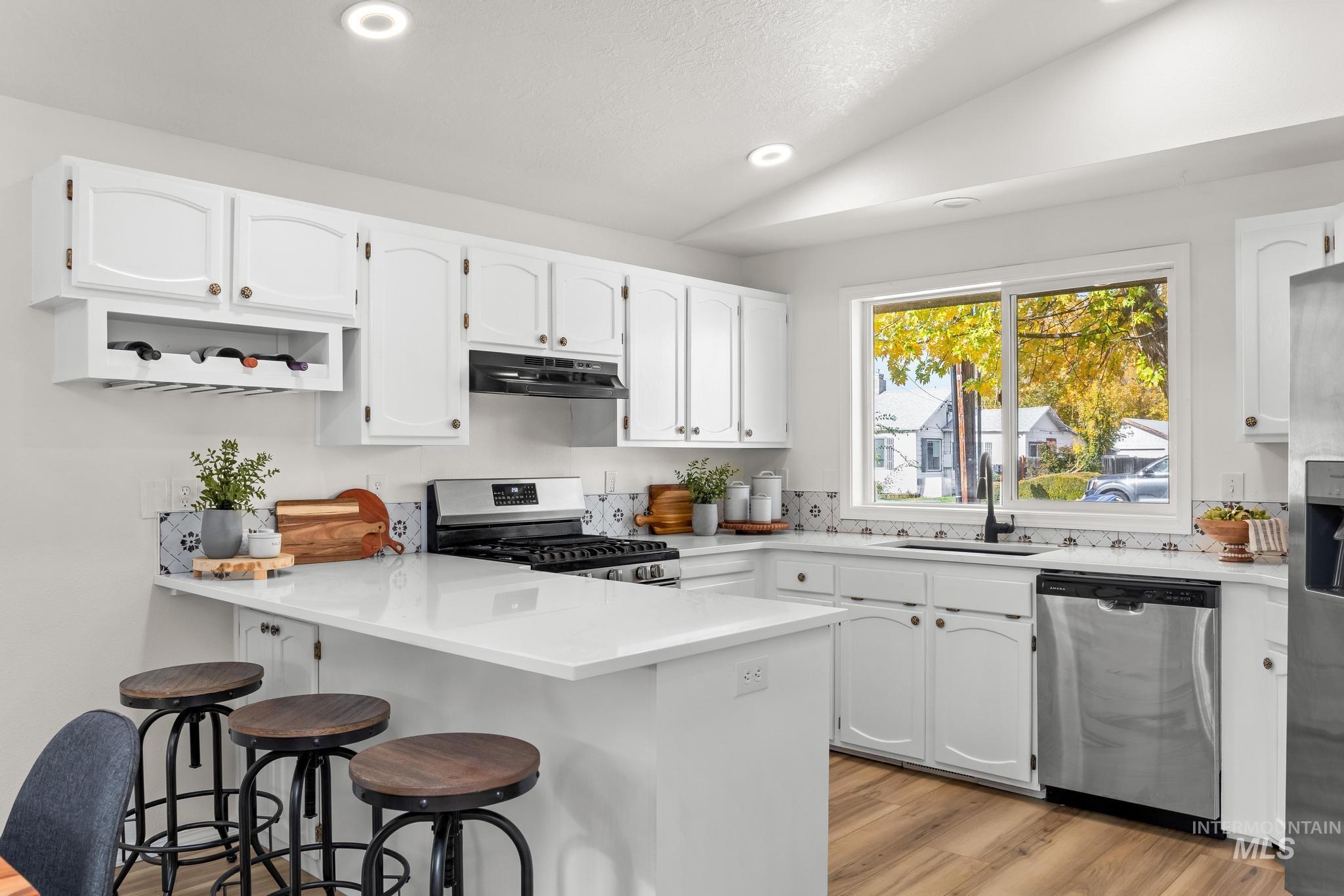 Kitchen with lofted ceiling, a peninsula, white cabinetry, stainless steel appliances, and light wood finished floors