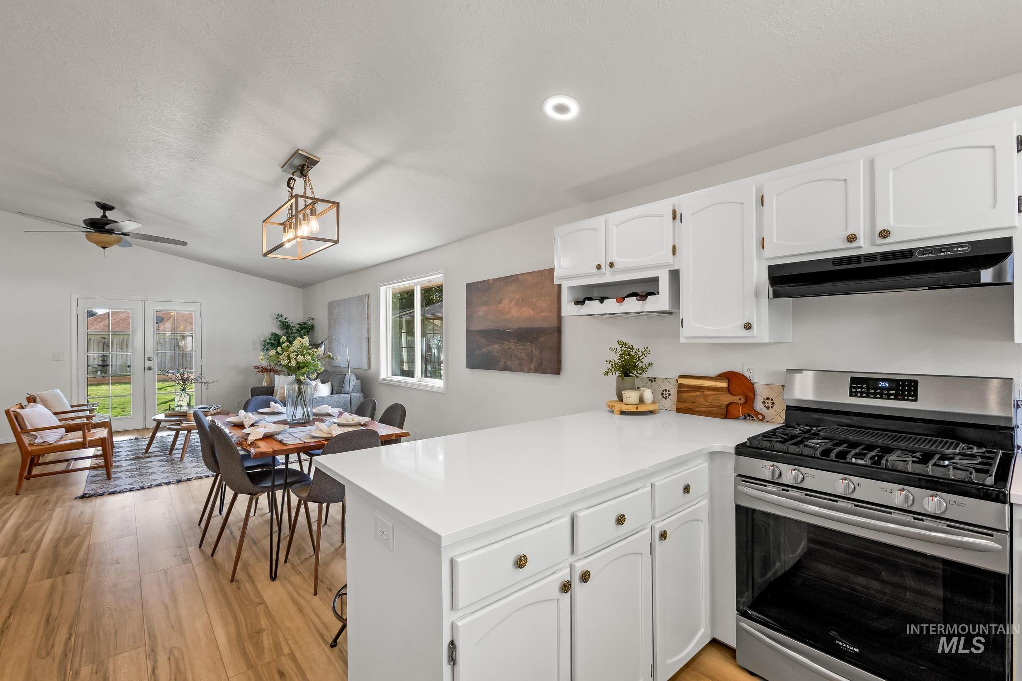 Kitchen with stainless steel gas stove, white cabinetry, light wood-style floors, open floor plan, and lofted ceiling
