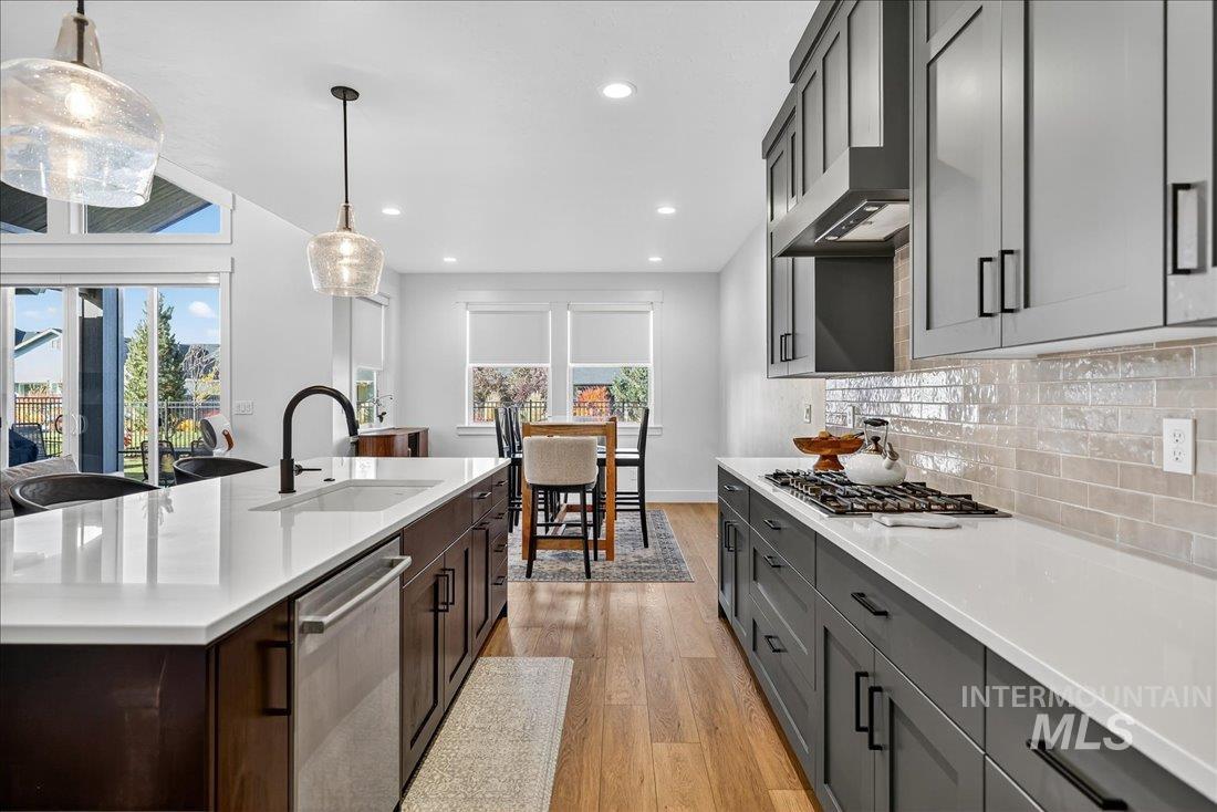 Kitchen with light wood-type flooring, backsplash, stainless steel appliances, pendant lighting, and healthy amount of natural light