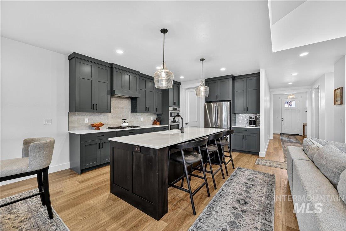 Kitchen with a kitchen bar, light wood-style floors, a center island with sink, tasteful backsplash, and decorative light fixtures