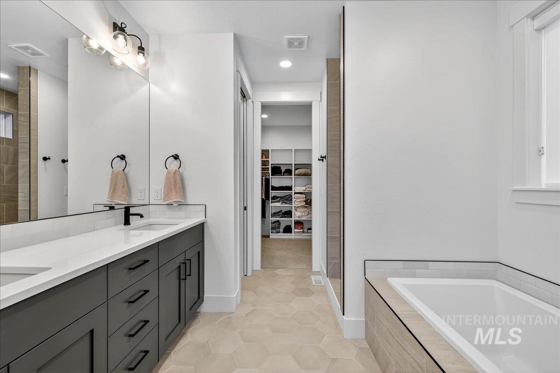 Bathroom featuring double vanity, a spacious closet, a bath, light tile patterned floors, and recessed lighting