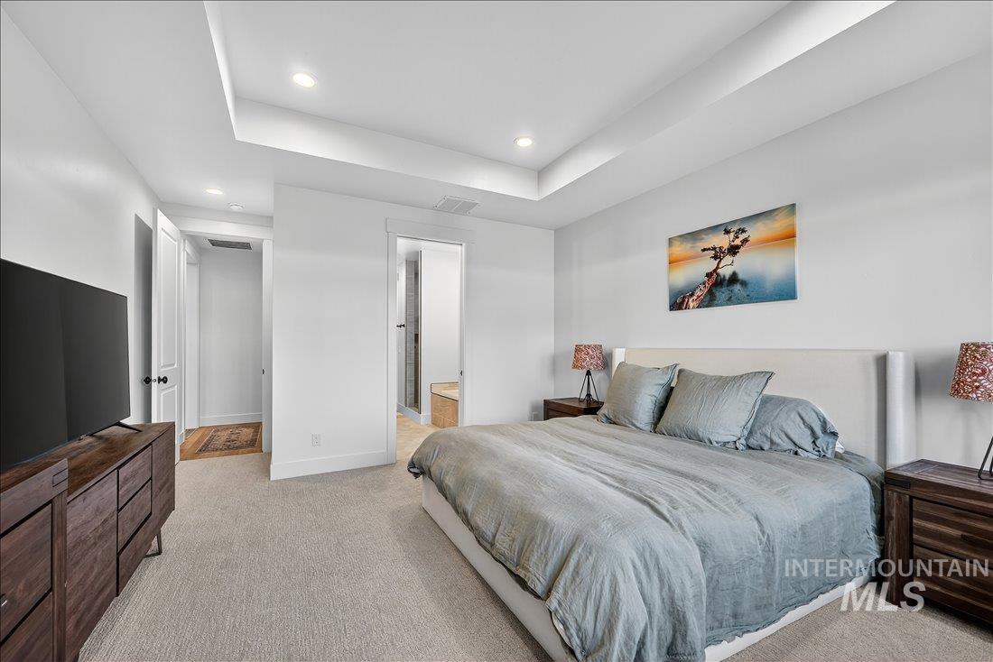 Bedroom featuring a tray ceiling, light colored carpet, connected bathroom, and recessed lighting