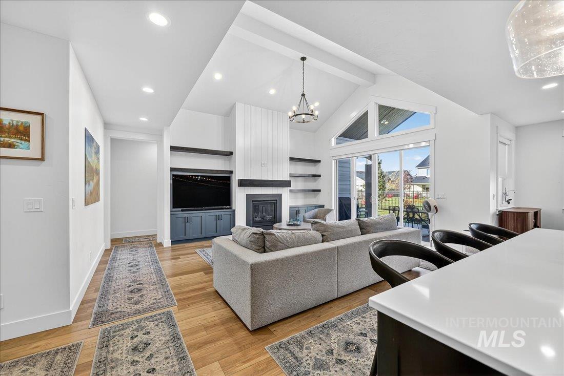 Living area with a fireplace, light wood finished floors, high vaulted ceiling, a chandelier, and recessed lighting
