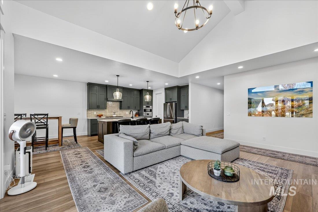 Living area with light wood finished floors, high vaulted ceiling, recessed lighting, a chandelier, and beam ceiling