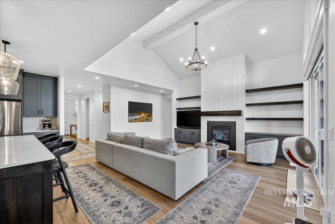Living room featuring beamed ceiling, a chandelier, light wood-type flooring, a large fireplace, and recessed lighting