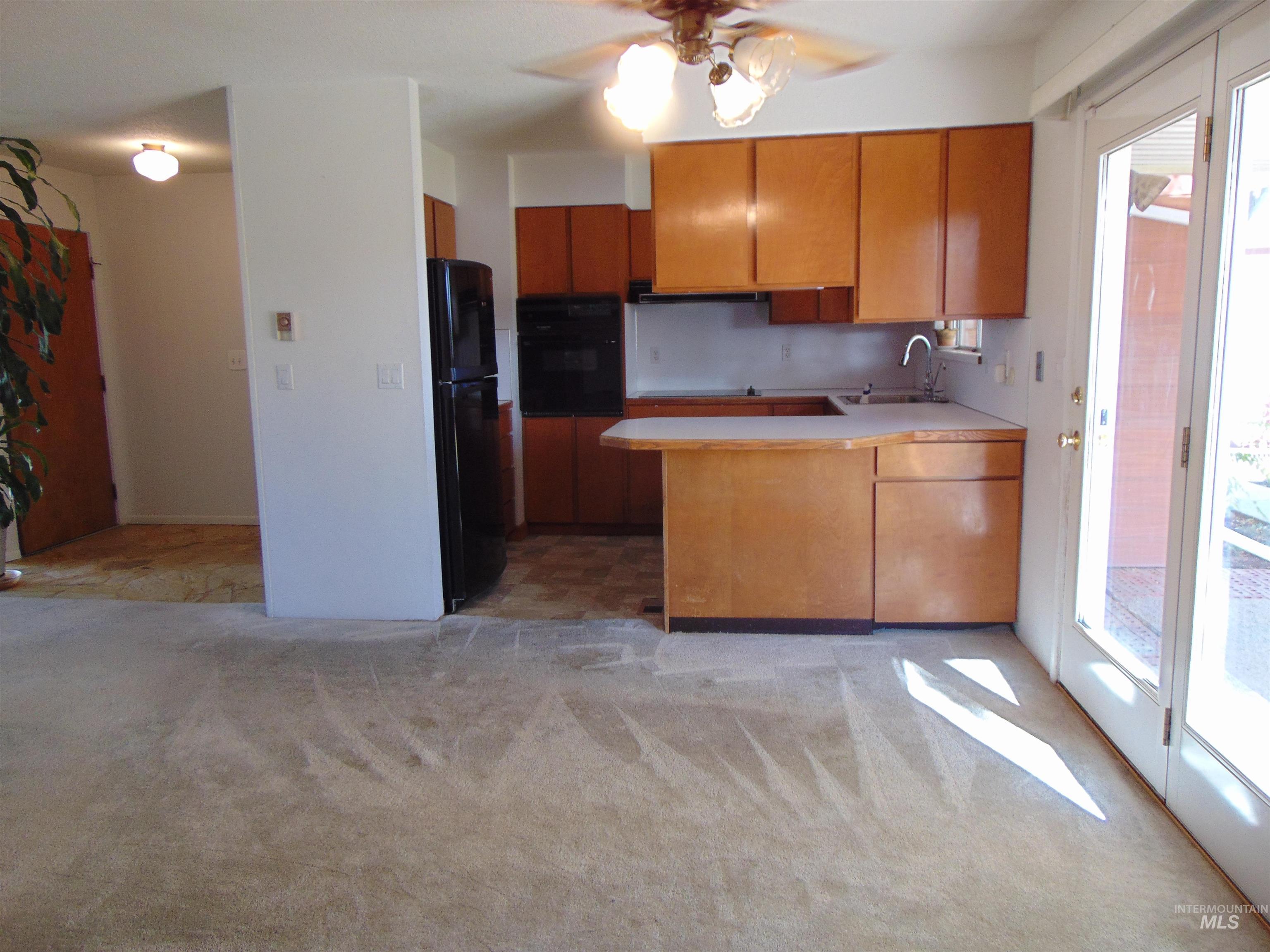 Kitchen featuring brown cabinetry, a peninsula, light countertops, black appliances, and a ceiling fan