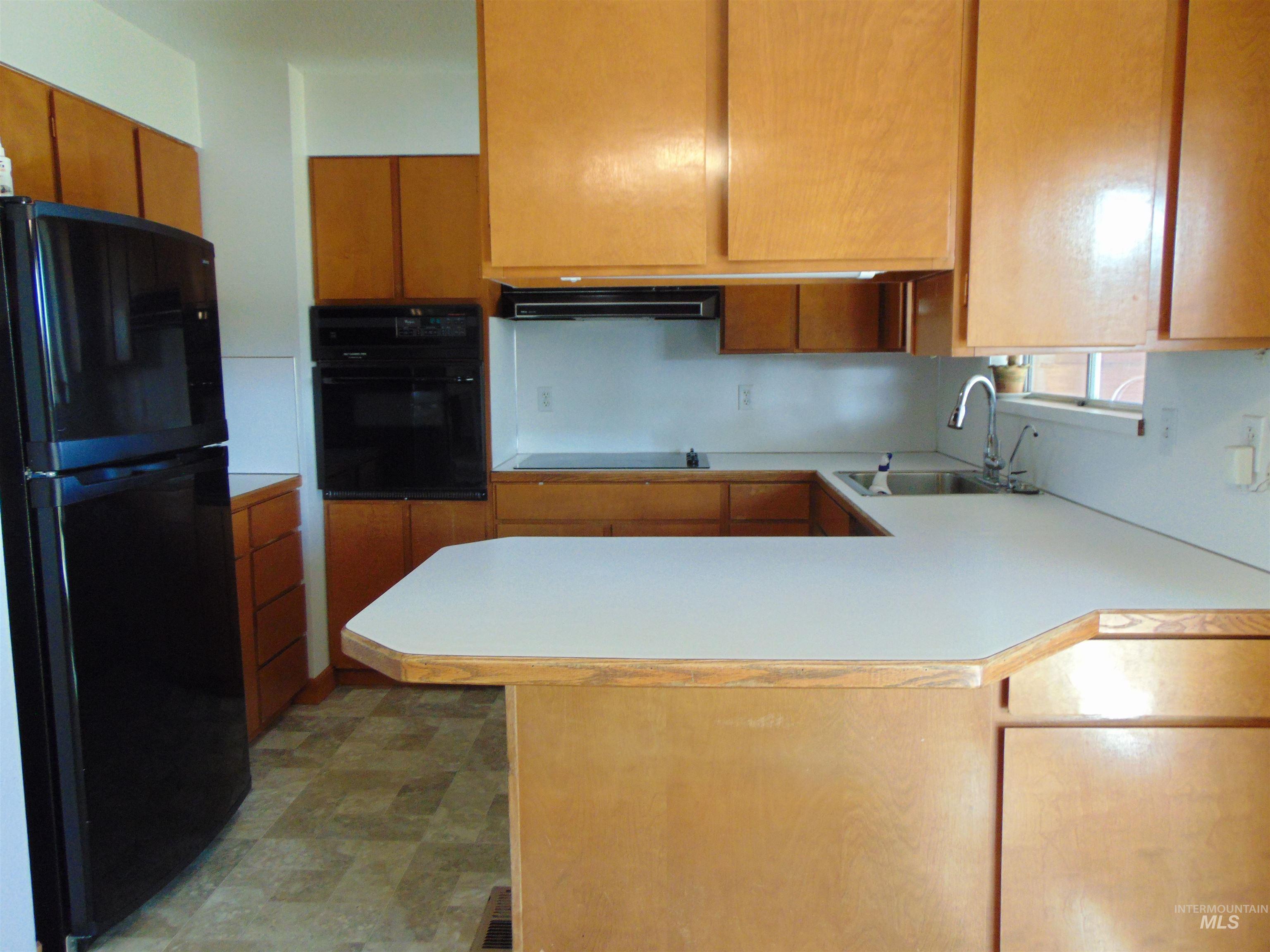 Kitchen with black appliances, light countertops, a peninsula, and brown cabinetry