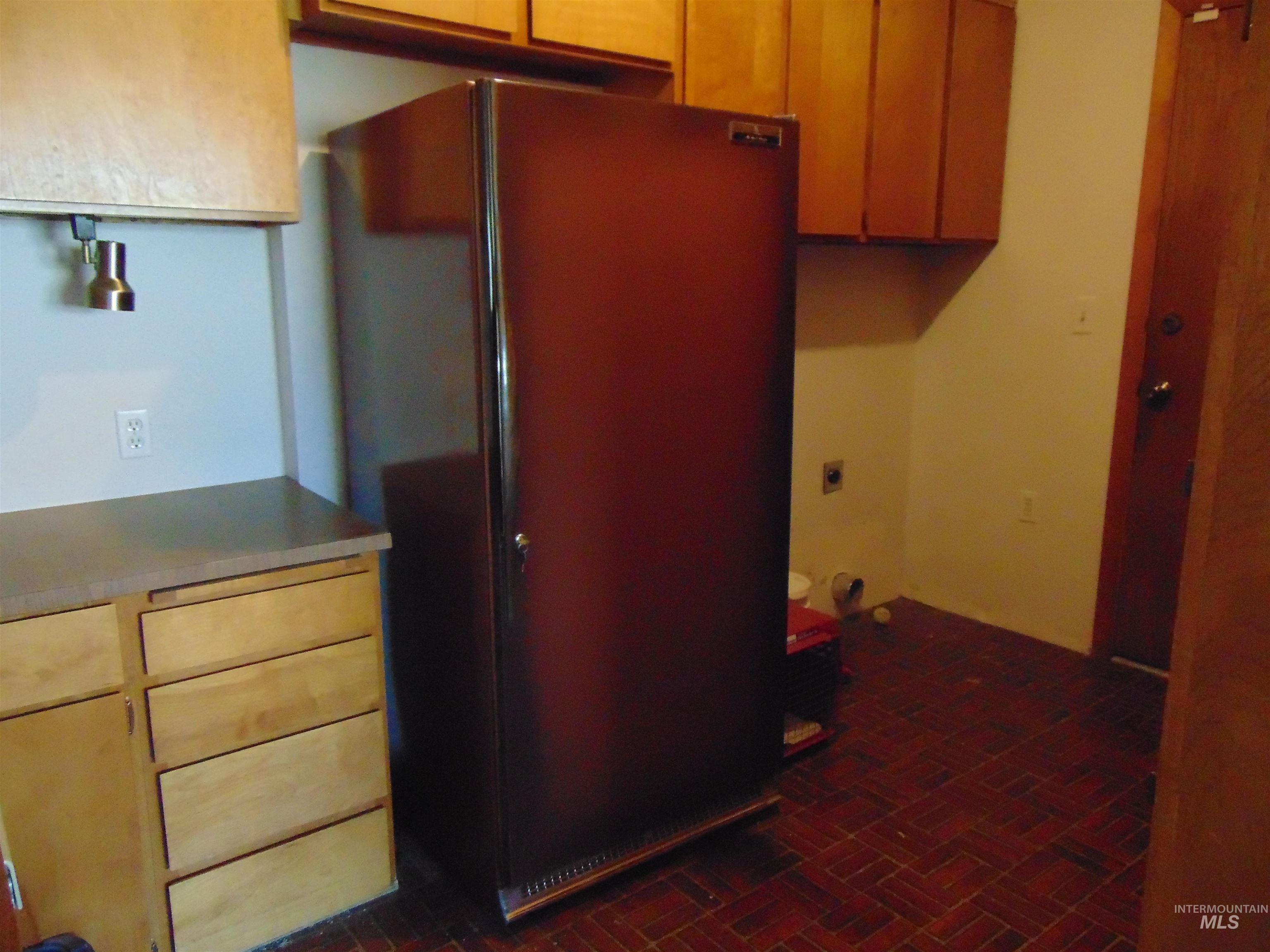 Kitchen featuring freestanding refrigerator, brick patterned flooring, light countertops, and brown cabinets