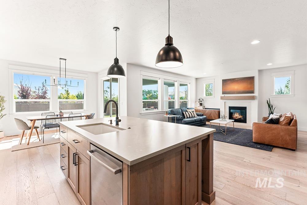 Kitchen with a glass covered fireplace, light wood-type flooring, hanging light fixtures, dishwasher, and open floor plan