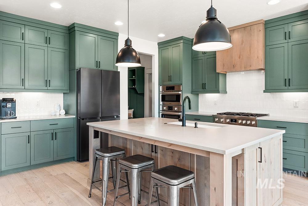 Kitchen featuring green cabinetry, backsplash, light wood-type flooring, appliances with stainless steel finishes, and recessed lighting